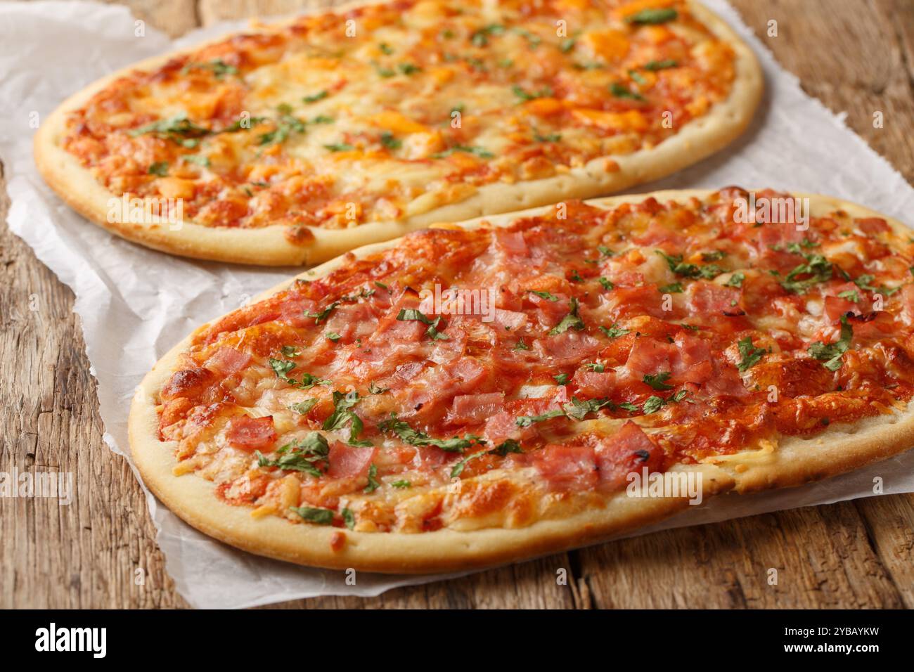 Köstliche römische Pizza mit Käse, Schinken und Tomatensauce in Nahaufnahme auf Pergament auf Holztisch. Horizontal Stockfoto