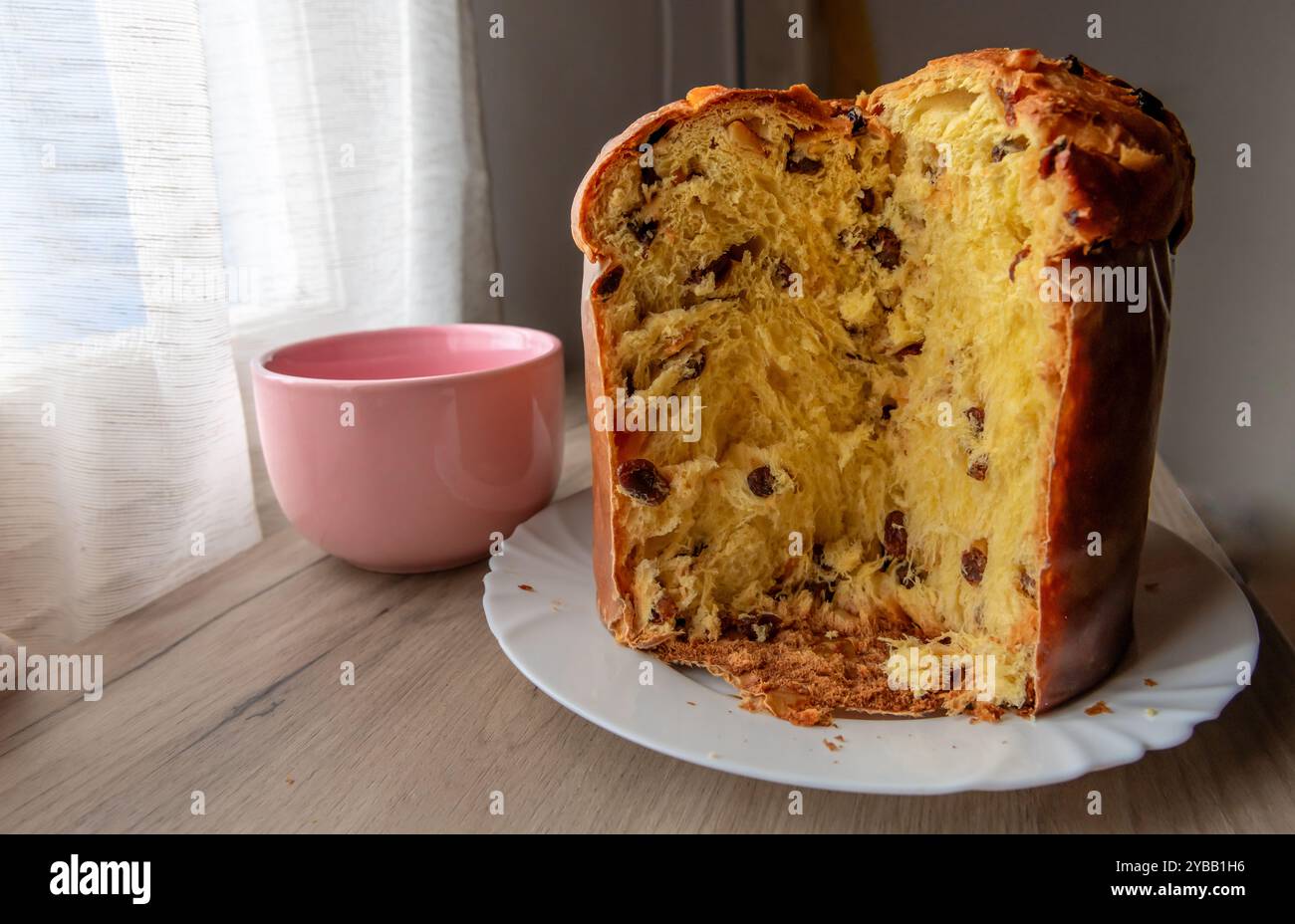 Ein italienischer Panettone, Weihnachtskuchen, mit einer Scheibe geschnitten, auf einem Sideboard mit einer Tasse Tee oder Kaffee. Stockfoto