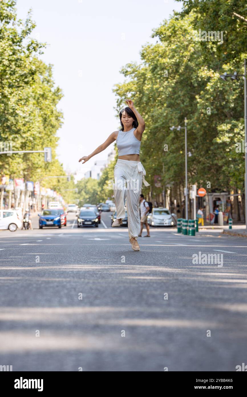 Sorglose Frau tanzt glücklich in einer verkehrsfreien Straße und genießt urbane Freiheit und Freude an einem sonnigen Sommertag Stockfoto