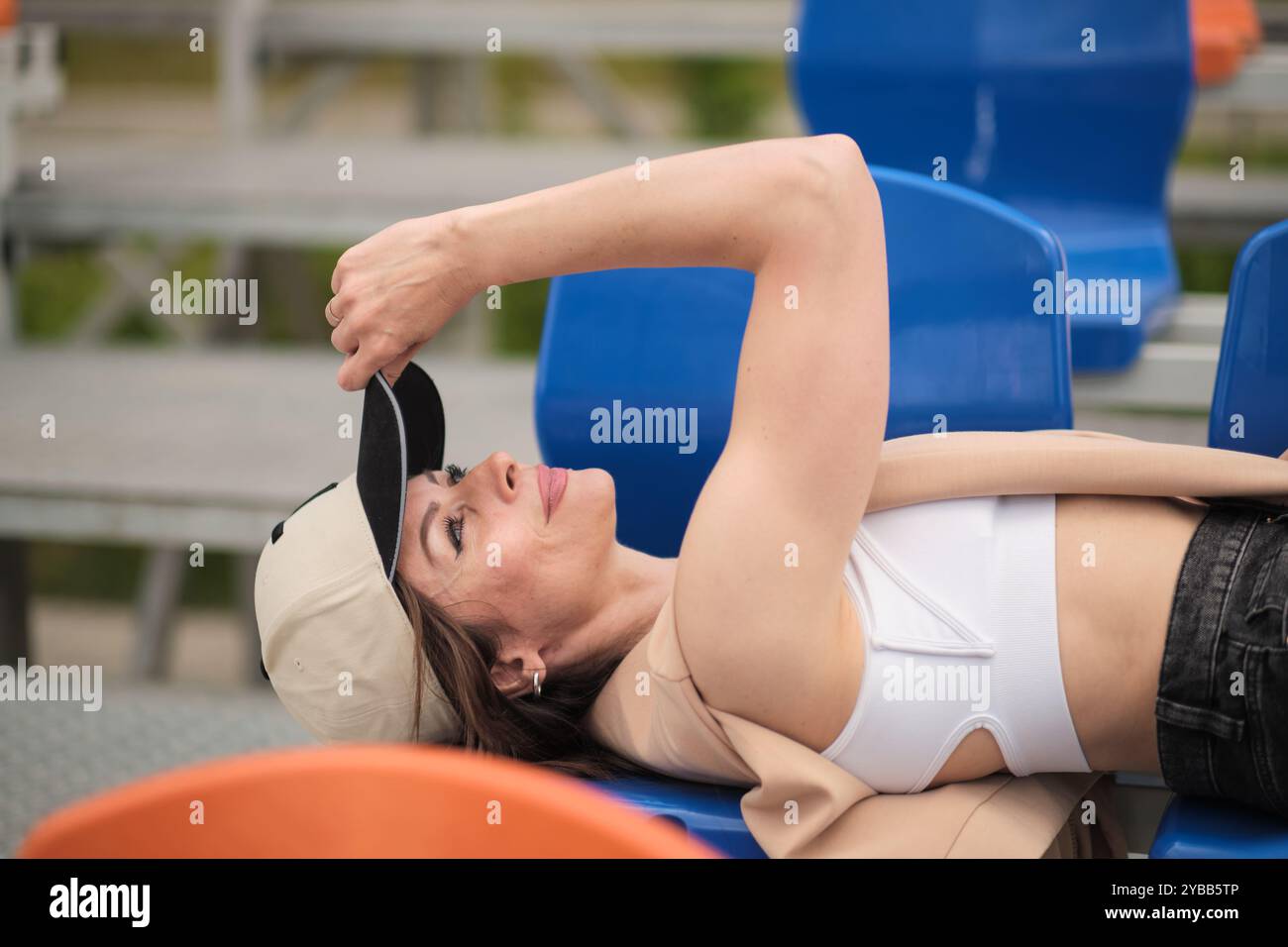 oman liegt auf blauen Sitzen, passt ihre Kappe mit einem zufriedenen Ausdruck an und zeigt lässigen Komfort. Konzept: Demonstrieren, wie man Zeit findet Stockfoto