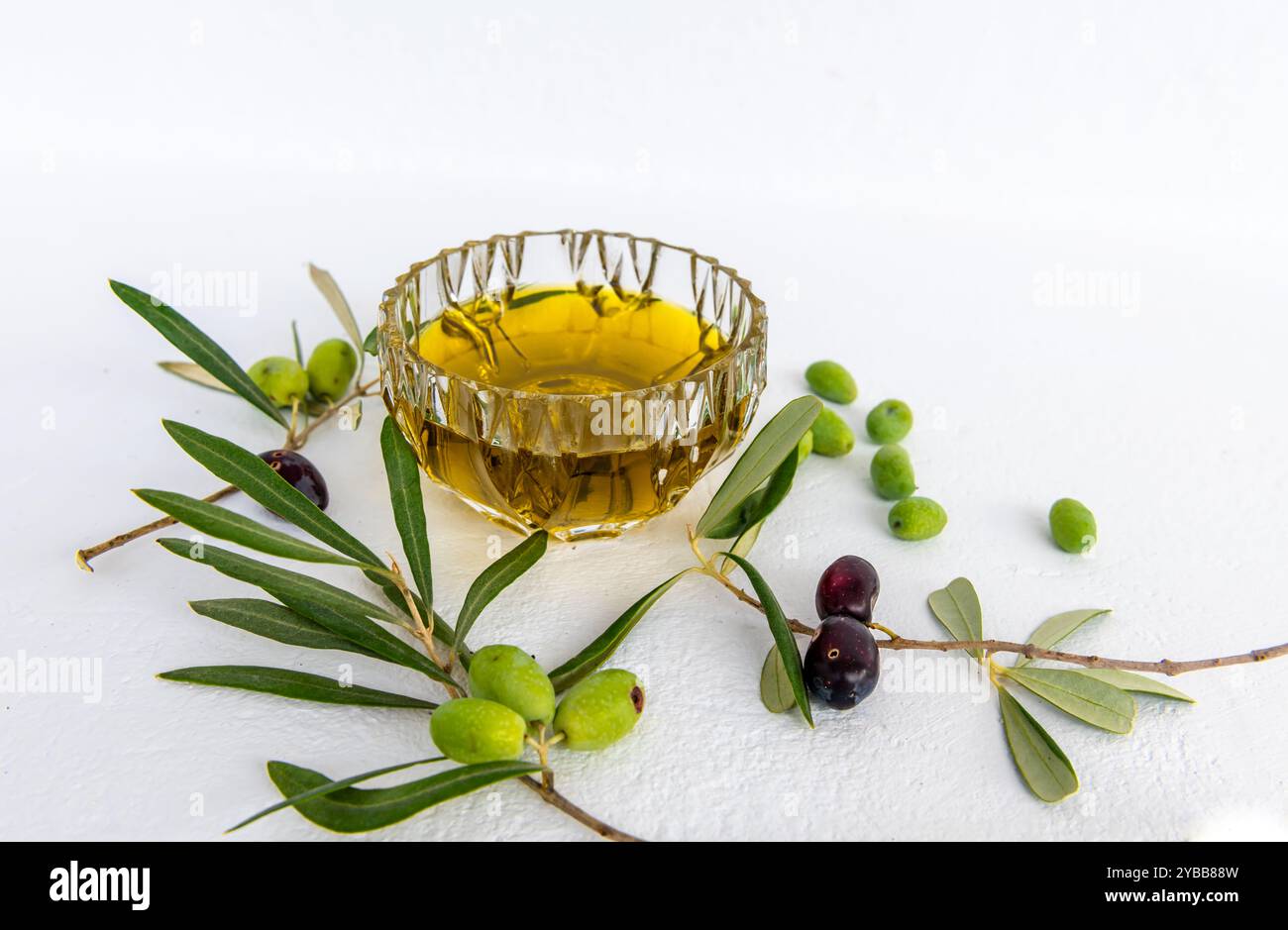 Olivenöl in einer Kristallglasschale, grüne und schwarze Oliven in Zweigen und lose grüne Oliven, isoliert in weiß. Stockfoto