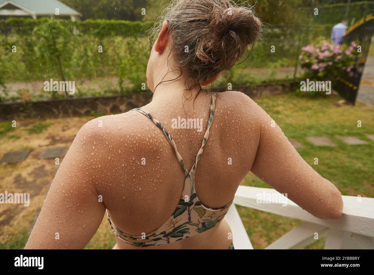 Wassertropfen auf dem Rücken der Frau im Bikinitop im Sommer-Garten Stockfoto