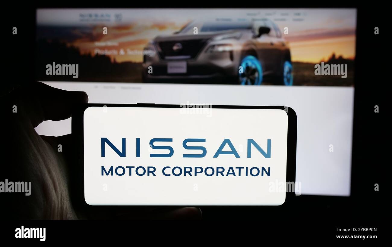 Person, die ein Mobiltelefon mit dem Logo der japanischen Firma Nissan Motor Corporation auf dem Bildschirm vor der Webseite hält. Schwerpunkt auf dem Display des Telefons. Stockfoto