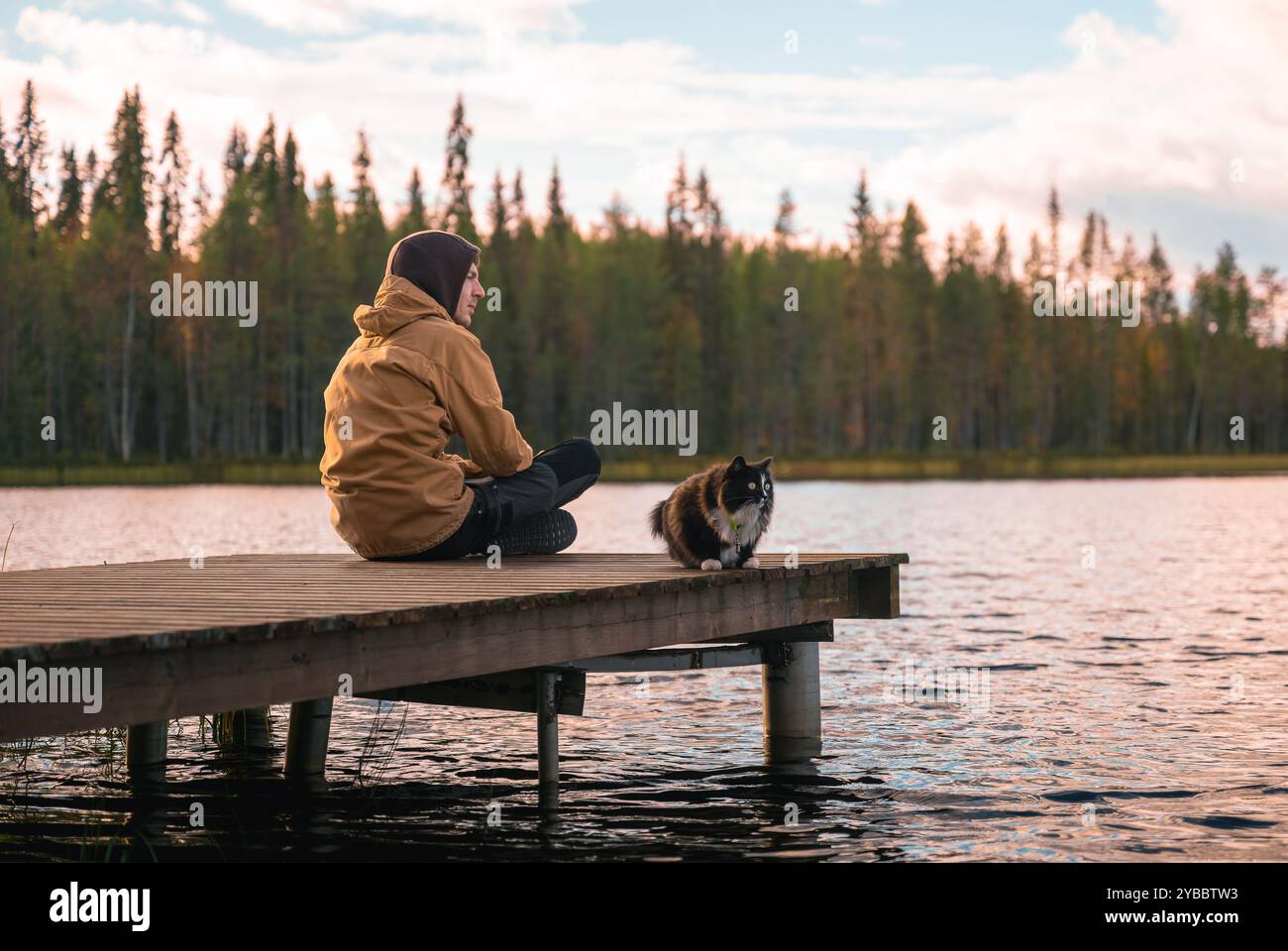 Mann mit Katze, der auf einem Holzsteg sitzt Stockfoto