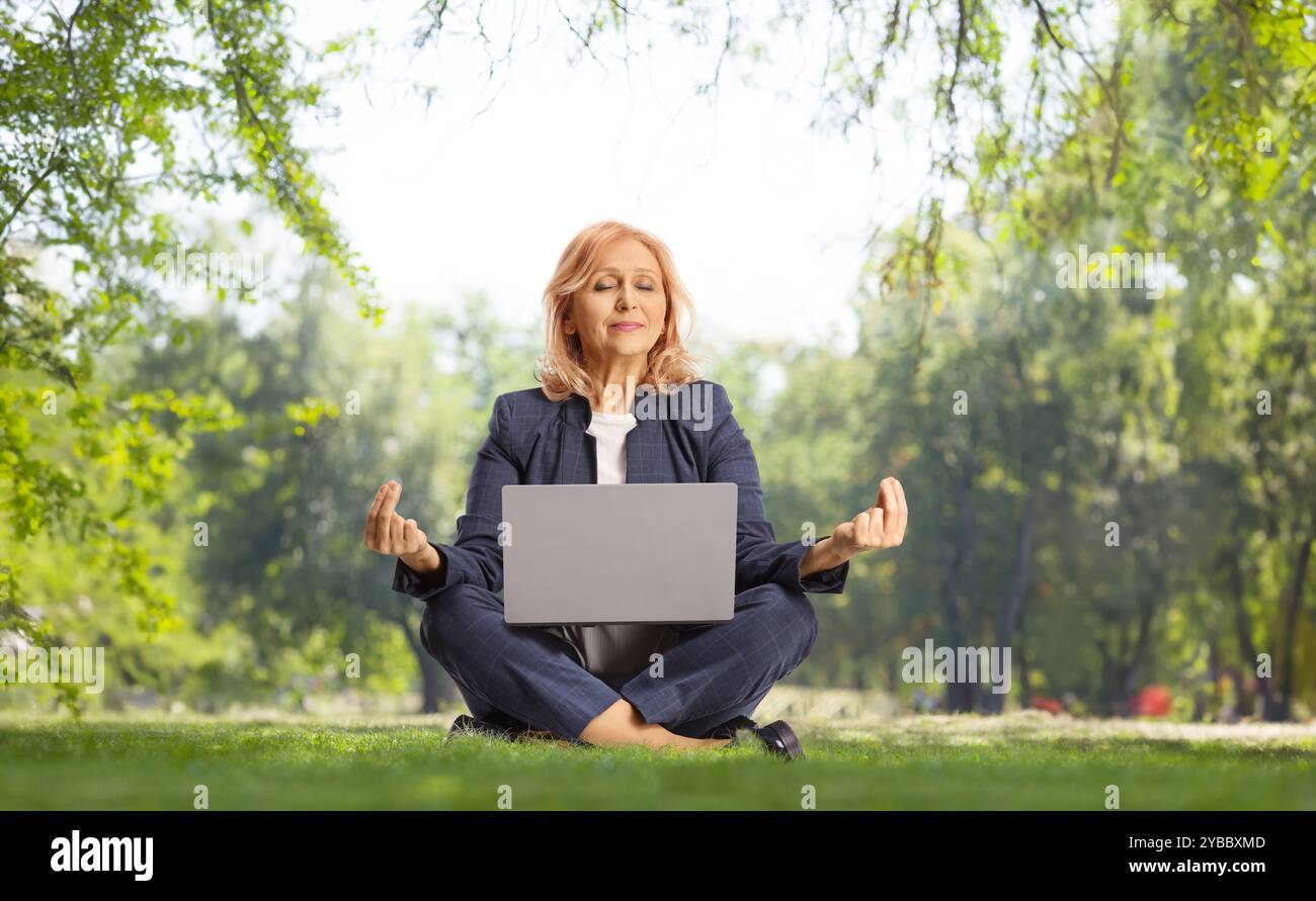 Geschäftsfrau mit einem Laptop, der in Meditationspose auf Gras sitzt Stockfoto