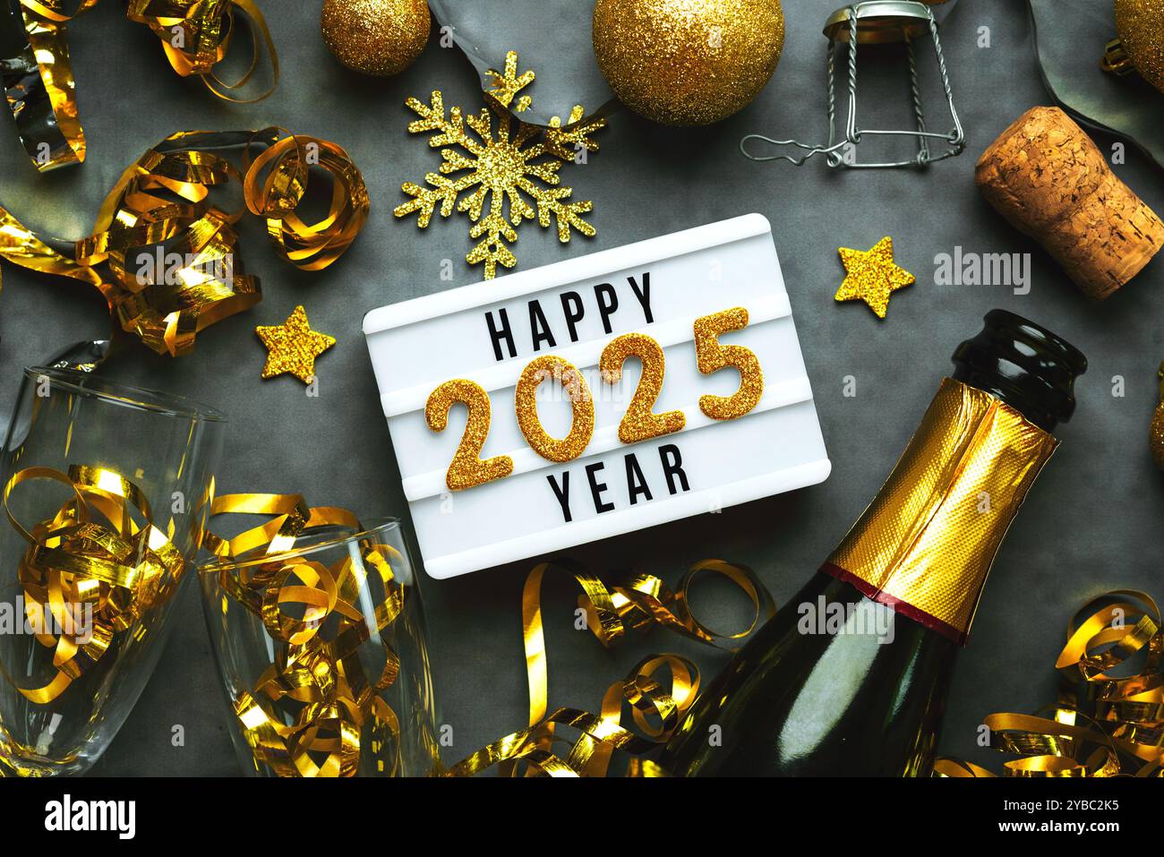 Happy New Year 2025.Top Blick auf Leuchtkasten mit dem Wort Happy New Year 2025, Flasche Champagner und Kristallgläser über dunklem Hintergrund. Silvester Stockfoto