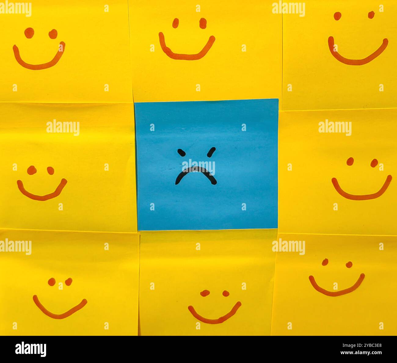 Emotionaler Kontrast. Blauer Haftnotiz mit Angry Expression, umgeben von gelben Smiley-Gesichtern. Stockfoto