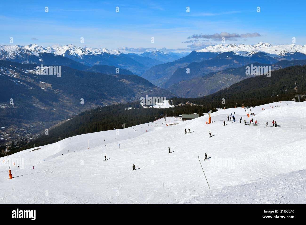 Blick auf ein Bergtal vom Skigebiet Meribel in den französischen Alpen. Skifahrer und Snowboarder, die eine breite Piste hinter den drei Tälern abfahren Stockfoto