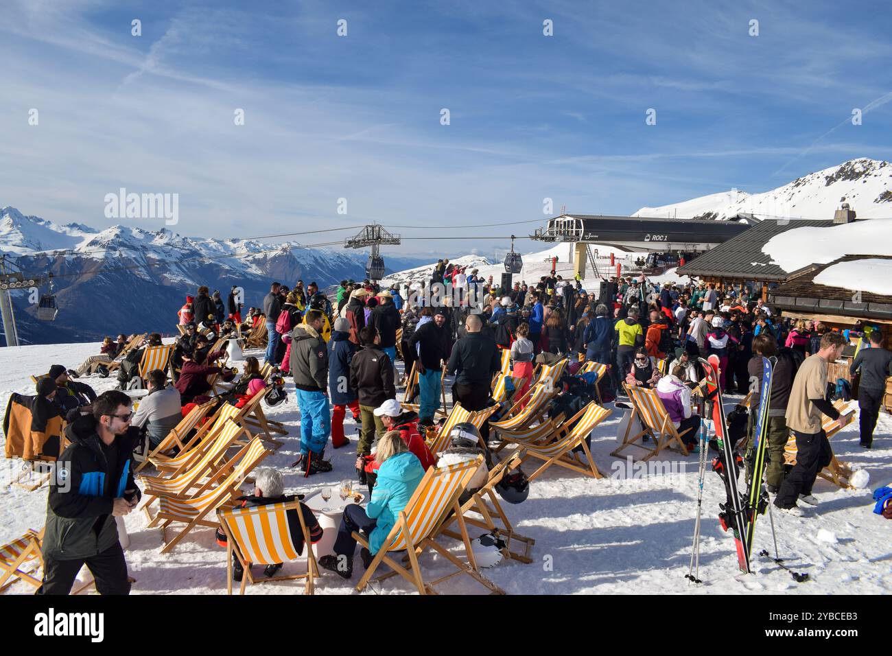 Les Menuires - 13. März 2024: Apres Ski Party an einer aktiven Skipiste im französischen Skigebiet Les Menuires. Skifahrer trinken neben schneebedeckten Bergen. Stockfoto