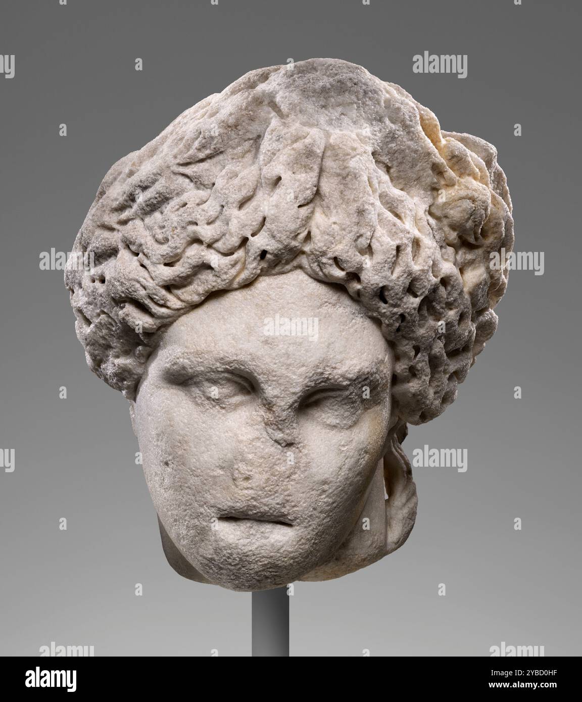 Kopf des Apollo (Lykeios-Cyren-Typ), 2. Jahrhundert n. Chr. zusätzliche Info: Trotz der stark abgenutzten Gesichtszüge auf diesem überlebensgroßen Kopf kann das Thema als Darstellung von Apollo identifiziert werden. Drei Details sichern diese Identifikation: Die volle Frisur mit einem nach oben gedrehten zentralen Zopf, die nach unten geneigte Kopfpartie und die noch sichtbaren Überreste einer Hand, die sich lässig über den Kopf gelegt hat. Dies sind die Standardmerkmale des weit verbreiteten skulpturalen Typs Apollo Lykeios, und dieser Kopf ist besonders nah an einem Subtyp, der als Apollo von Cyrene bekannt ist. In t Stockfoto