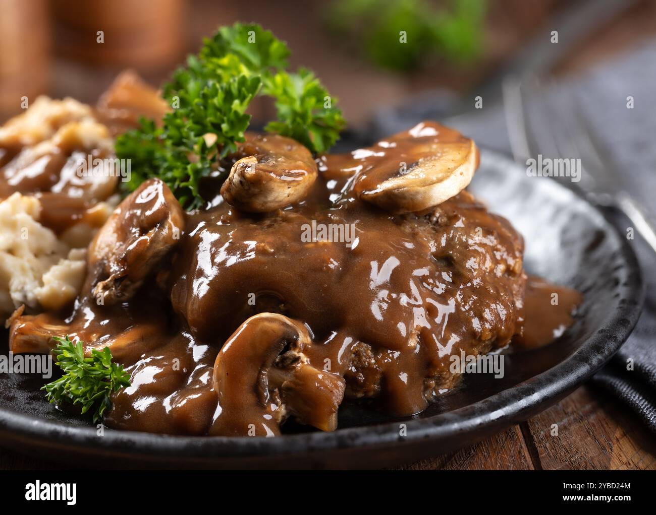 Salisbury-Steak mit Pilzsoße garniert mit Petersilie und Kartoffelpüree auf einem schwarzen Teller Stockfoto