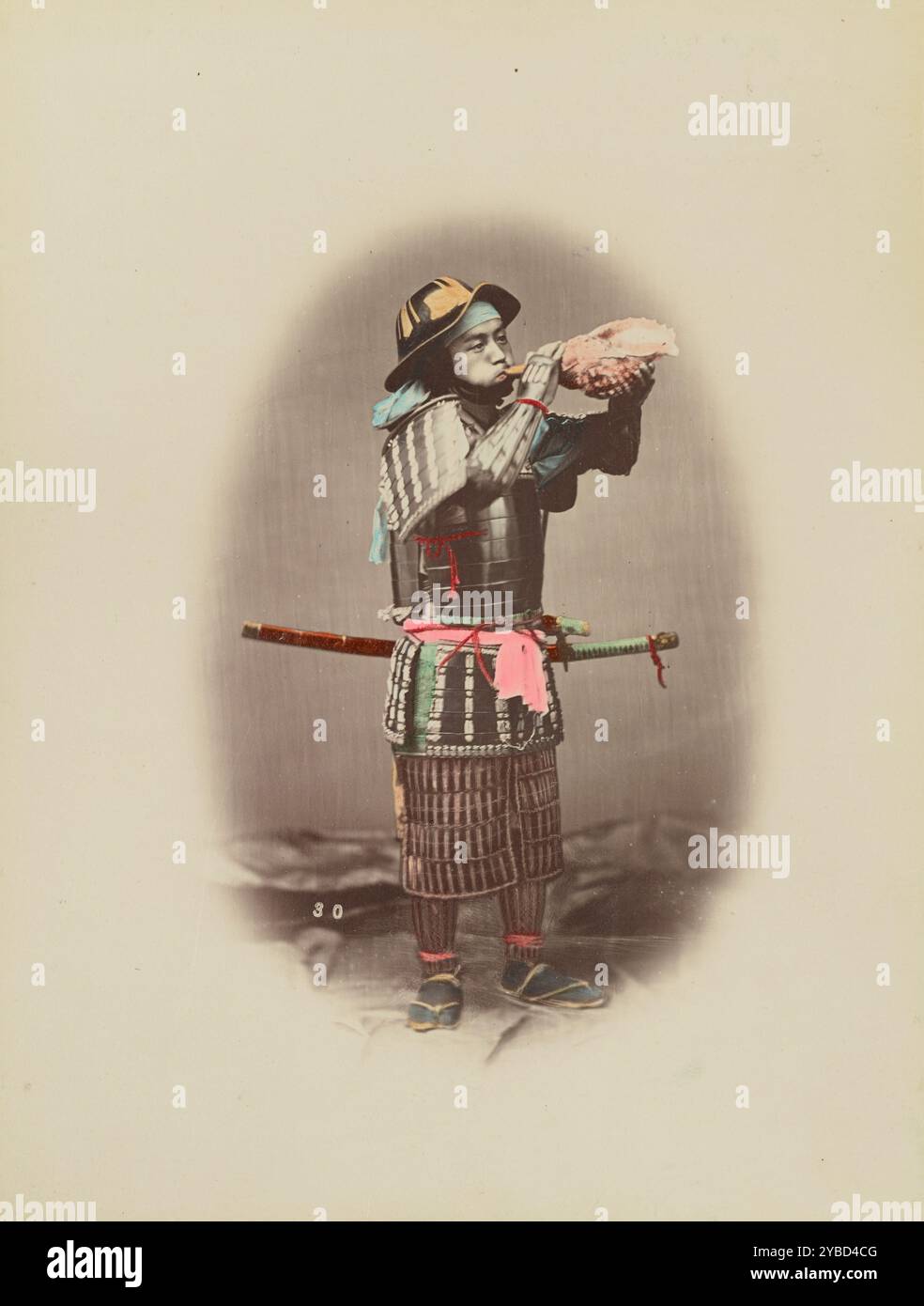 Samurai in Rüstung, 1870er-1890er Jahre Ein Mann mit traditioneller Rüstung, der in eine große Schale bläst. Stockfoto