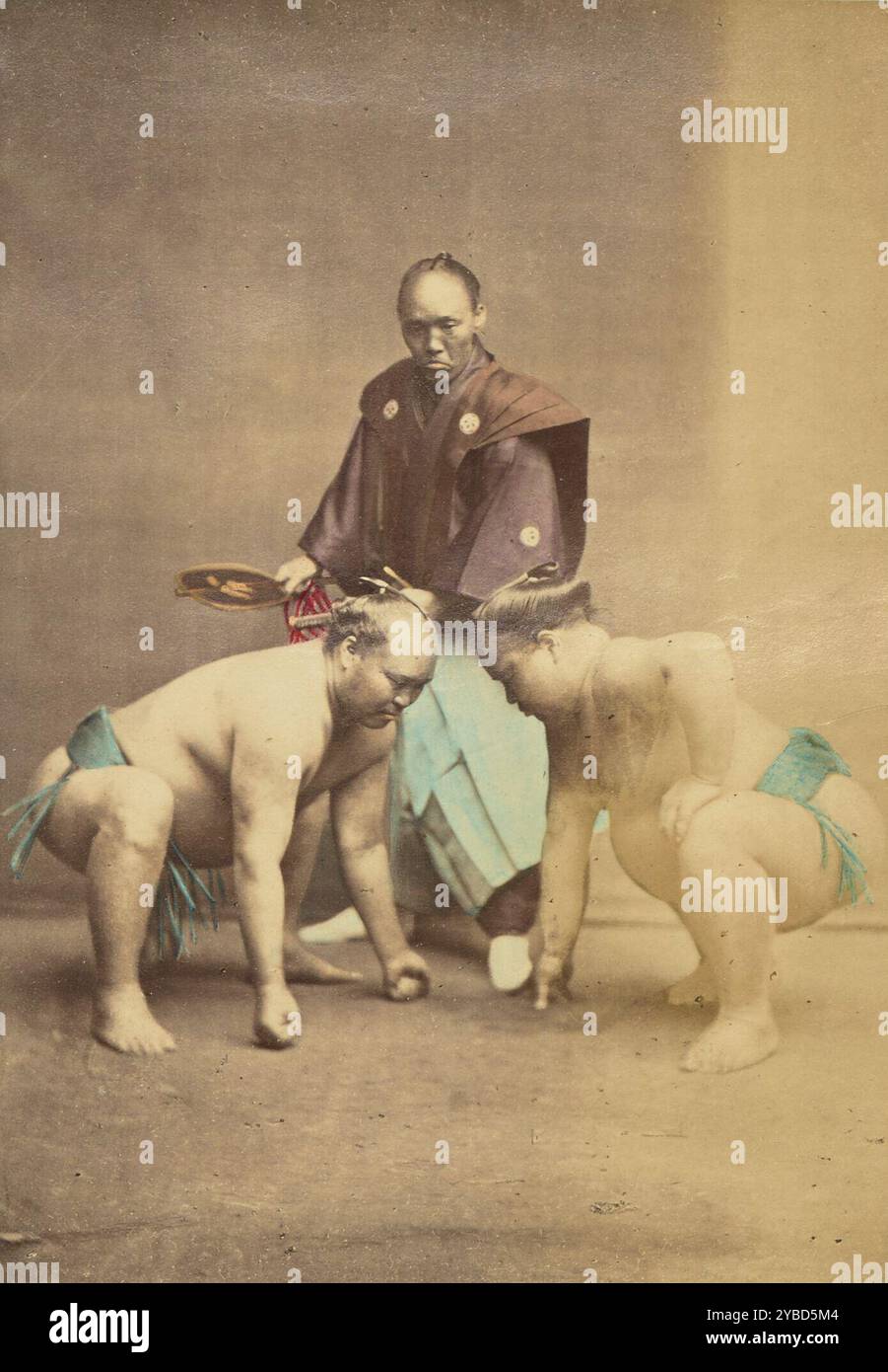 Zwei japanische Sumo-Wrestler posierten mit Schiedsrichter, 1868–1880. Porträt zweier Sumo-Wrestler, die sich in gehockten Positionen gegenüberstehen, mit einem gyoji oder Schiedsrichter, der dazwischen steht. Stockfoto