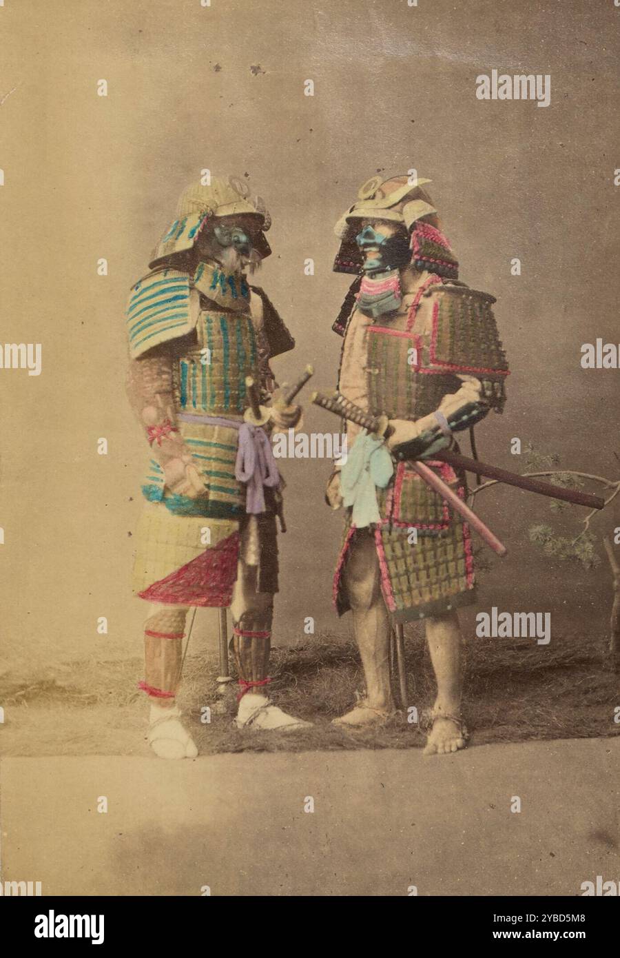Zwei japanische Krieger in vollen Kostümen, 1868-1880. Studio-Porträt von zwei Samurai in voller Rüstung. Die beiden Männer stehen einander gegenüber und liegen jeweils eine Hand auf einem Schwert, das an seiner Taille festgebunden ist. Gras unter den Füßen und ein kleiner Baum dienen als Stützen. Stockfoto