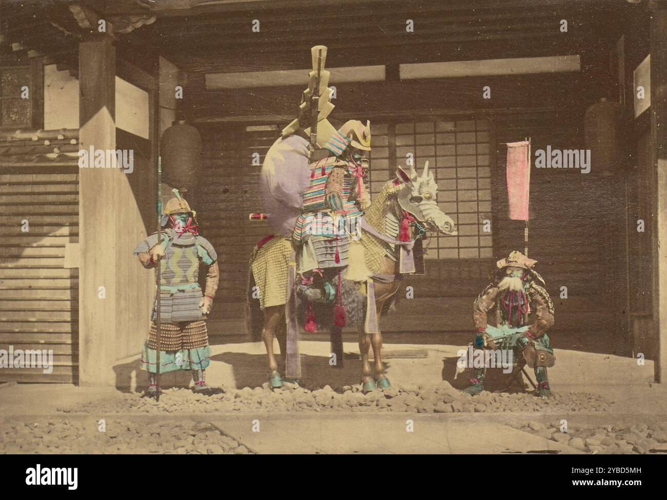 Drei japanische Krieger, 1868-1880. Porträt von drei Samurai in voller Rüstung, die vor einem Haus posieren. Der Krieger auf der linken Seite hält einen hohen Speer oder Stab, der Krieger in der Mitte sitzt auf einem Pferd im Profil, und der Krieger auf der rechten Seite auf einem kleinen Hocker. Das Pferd ist auch mit Rüstung versehen. Stockfoto