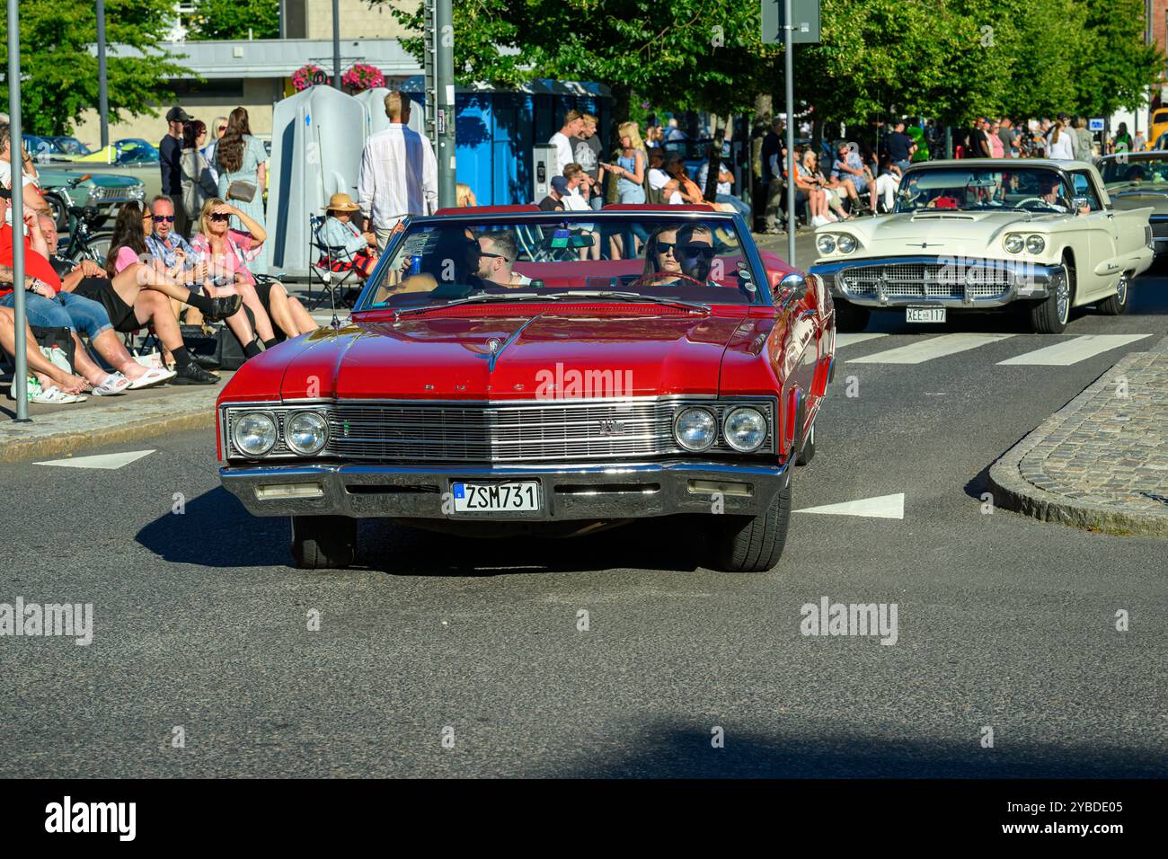 Eine lebhafte Parade von Oldtimern fährt durch eine geschäftige Straße, präsentiert Oldtimer und zieht begeisterte Besucher an. Es ist hell, sonnig Stockfoto