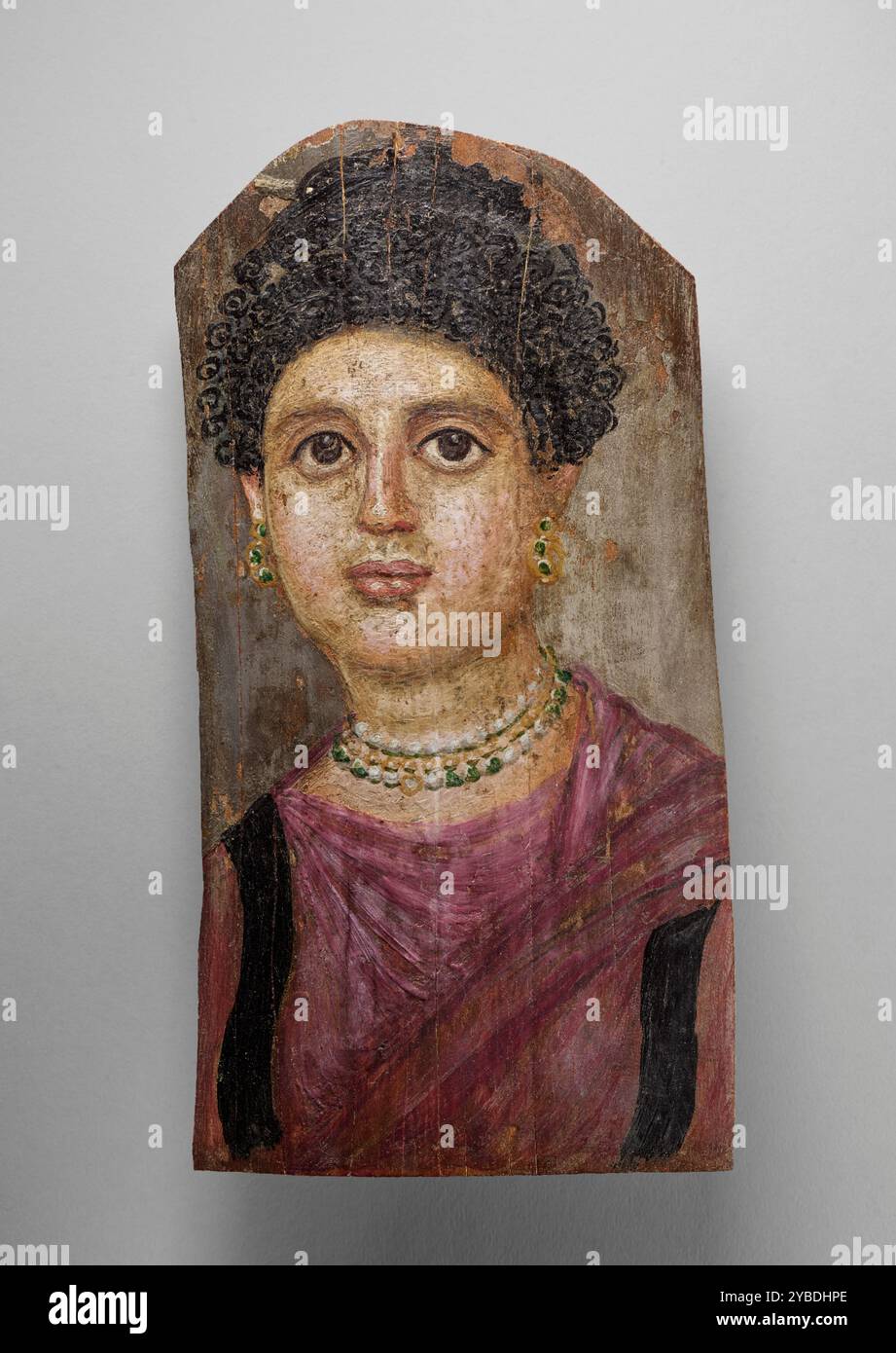 Mummy Portrait, A.D. 75-100. Zusätzliche Informationen: Dieses Porträt einer Frau präsentiert viele der charakteristischen Eigenschaften der romanisch-ägyptischen Grabtafeln. Der Stil ihres dunklen, lockigen Haares, das oben am Kopf zu einem losen Knoten gebunden war, war während der Flavianischen Zeit (68–96 n. Chr.) in Mode und trägt dazu bei, das Porträt auf die Jahre um diese Zeit zu datieren. Das Gesicht der Frau ist in Fleisch- und Lachstönen gemalt, der Hintergrund ist dunkelgrau, und ihr Kleid ist rosa-lavendelfarben (traditionell für weibliche Begräbnisporträts) mit schwarzen Clavi (gewebte Streifen), die vertikal an der Vorderseite verlaufen. Sie Stockfoto