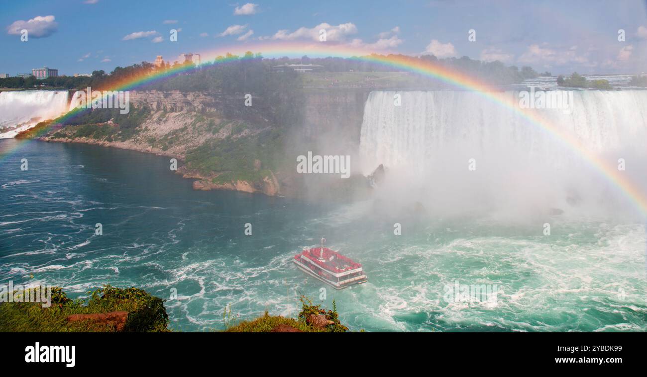 Ein Boot navigiert durch die Gewässer in der Nähe der Niagarafälle und zeigt einen wunderschönen Regenbogen über Ihnen. Stockfoto