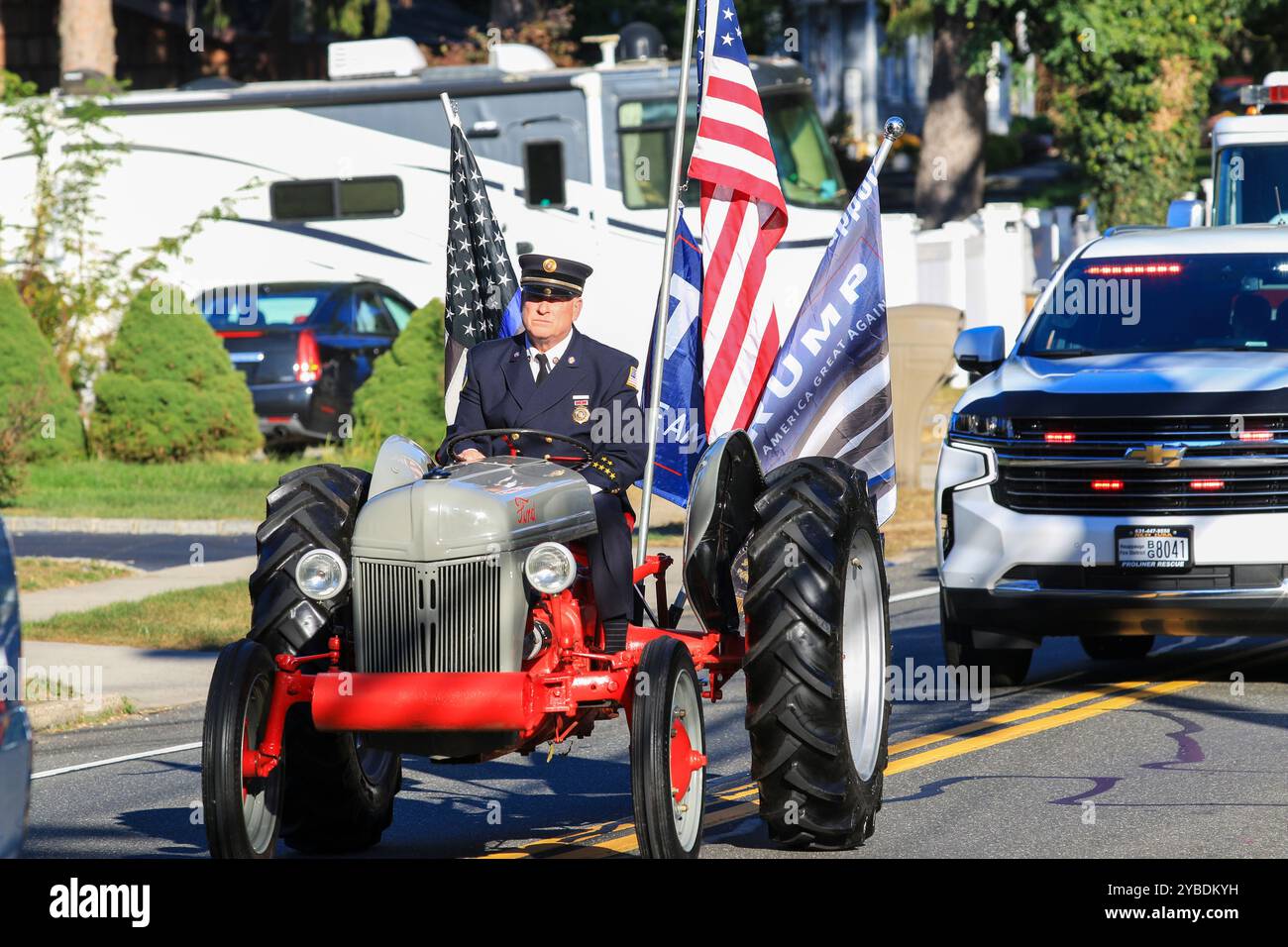 Hauppauge, New York, USA - 5. Oktober 2024: Ein örtlicher Freiwilliger Feuerwehrmann reitet stolz mit Fahnen in einem Traktor während der Heimfeierparade. Stockfoto
