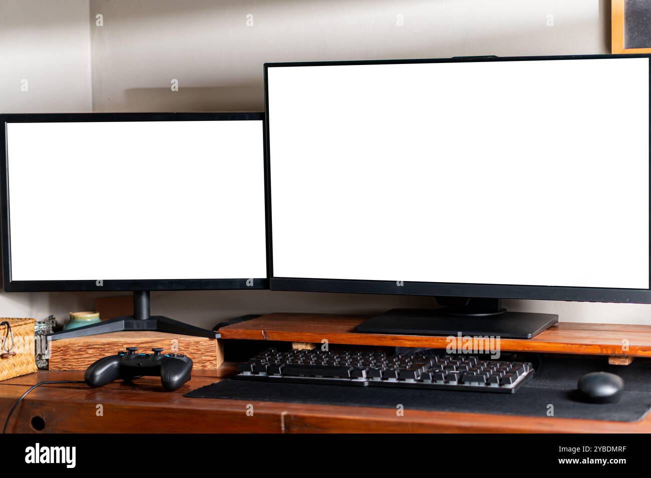 Zwei Computermonitore mit leeren Bildschirmen auf einem Holzpult, mit Tastatur und Gamecontroller. Stockfoto