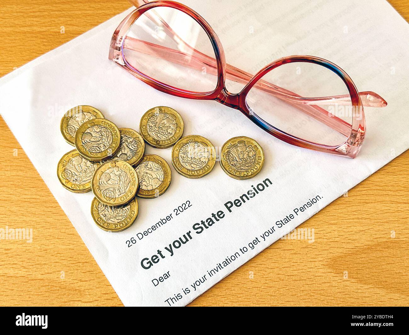 Ein offizieller Brief, in dem eine Person im Ruhestandsalter im Vereinigten Königreich mit einem Pfund Münzen und einer Lesebrille ihre Rente bekommen kann. - Smartphone-aufgenommenes Stockfoto