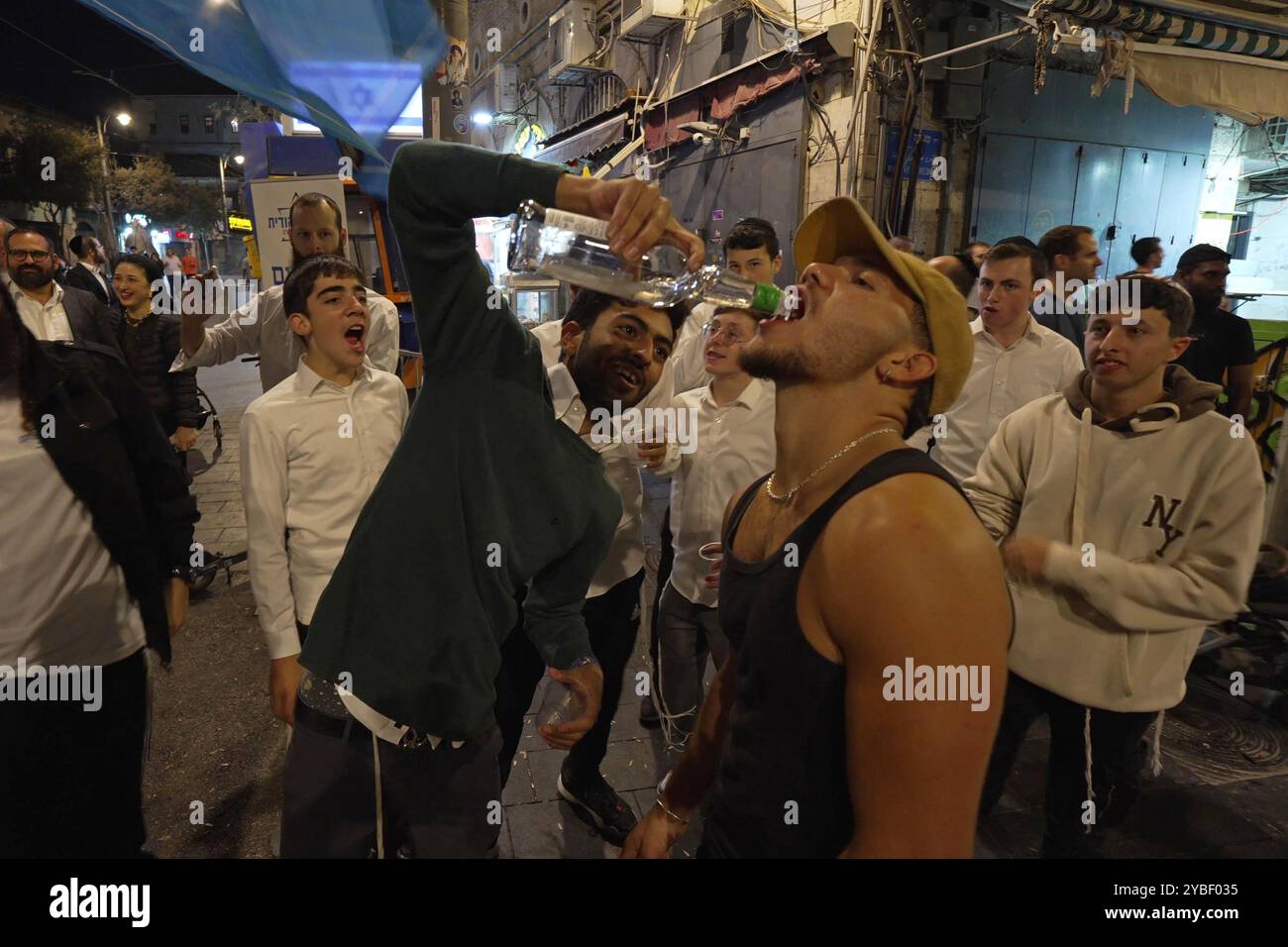 JERUSALEM - 17. OKTOBER: Ein Aktivist der rechtsextremen Partei Otzma Yehudit (jüdische Macht) gießt den Menschen auf dem Mahane Yehuda Markt ein alkoholisches Getränk in den Mund, während Israelis die Nachricht vom Tod des Hamas-Führers Yahya Sinwar am 17. Oktober 2024 in Jerusalem feiern. Israel bestätigte den Tod von Sinwar, dem Drahtzieher des Angriffs vom 7. Oktober, und nannte es einen großen Rückschlag für die palästinensische Gruppe, die es seit mehr als einem Jahr kämpft. Stockfoto