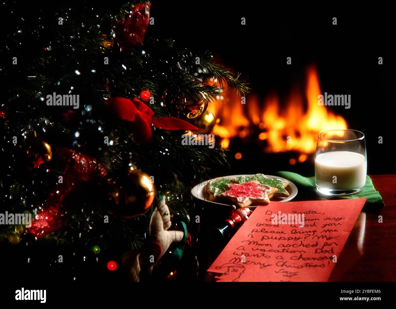 Eine gemütliche Weihnachtsszene mit Milch, Keksen und einem Brief an den Weihnachtsmann neben einem wunderschön dekorierten Baum und einem warmen Kamin Stockfoto