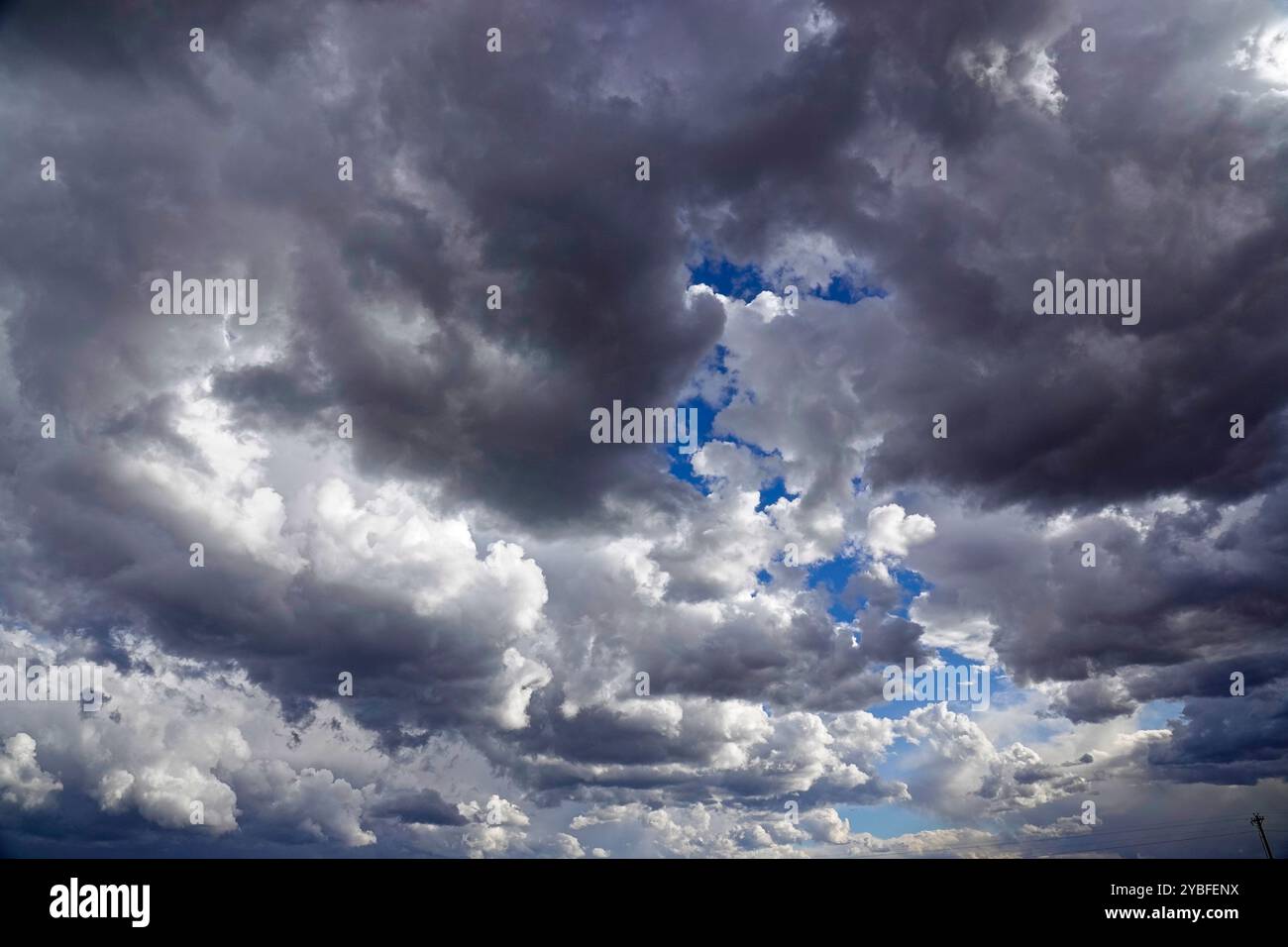 Über den Wolken erheben sich aufziehende Gewitterwolken, gefüllt mit verschiedenen Grau- und Weißtönen, die während der Nachmittagsstunden blaue Himmelsflecken enthüllen, Suggesti Stockfoto