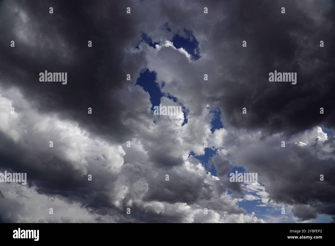 Über den Wolken erheben sich aufziehende Gewitterwolken, gefüllt mit verschiedenen Grau- und Weißtönen, die während der Nachmittagsstunden blaue Himmelsflecken enthüllen, Suggesti Stockfoto