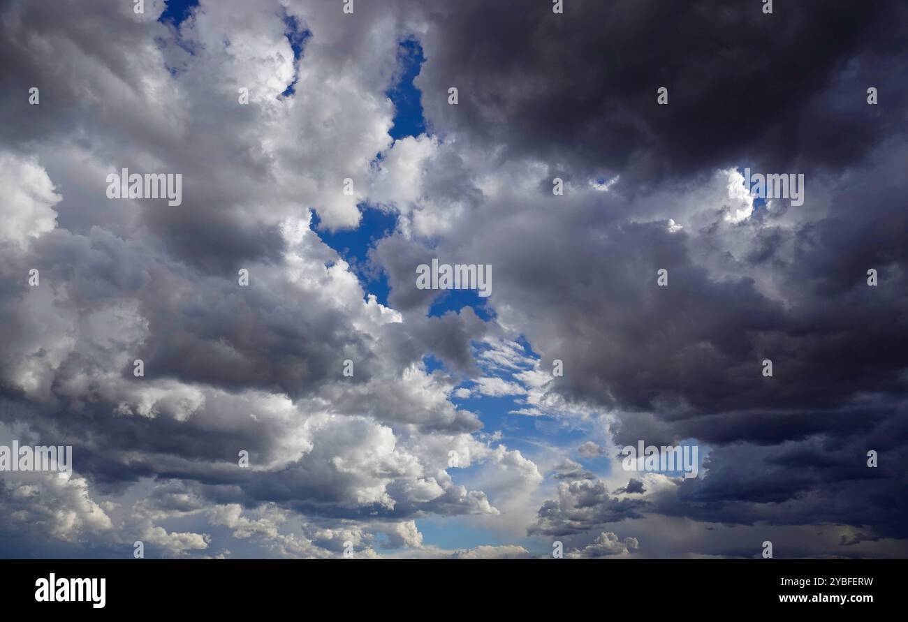 Über den Wolken erheben sich aufziehende Gewitterwolken, gefüllt mit verschiedenen Grau- und Weißtönen, die während der Nachmittagsstunden blaue Himmelsflecken enthüllen, Suggesti Stockfoto