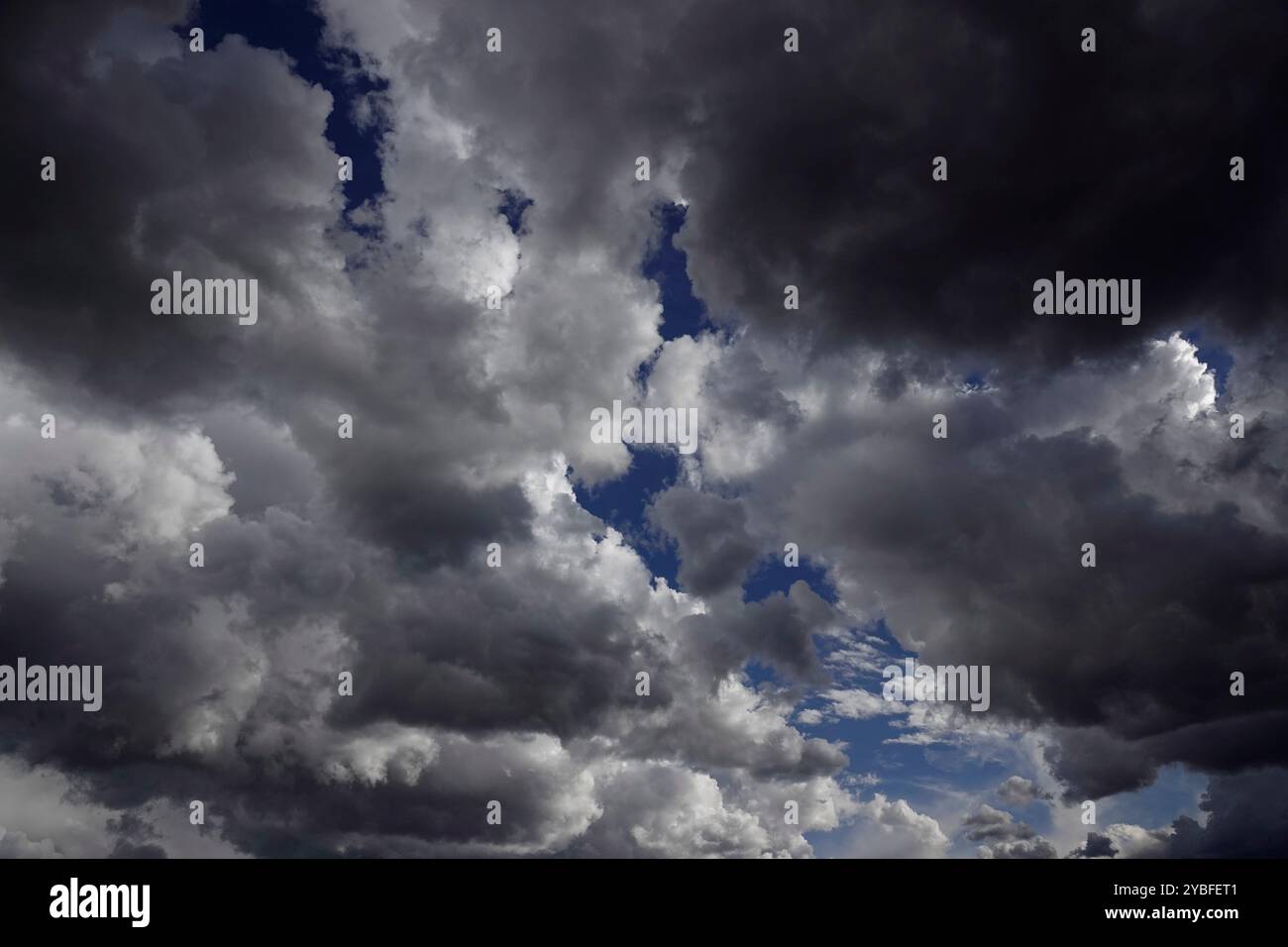 Über den Wolken erheben sich aufziehende Gewitterwolken, gefüllt mit verschiedenen Grau- und Weißtönen, die während der Nachmittagsstunden blaue Himmelsflecken enthüllen, Suggesti Stockfoto