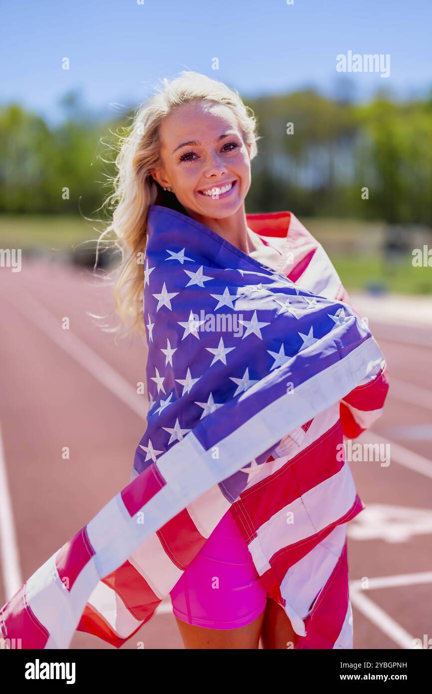 Stolze amerikanische Athletin schwenkt die US-Flagge und ehrt ihr Land nach einem triumphalen lokalen Rennstreckentreffen, das Patriotismus und Respekt verkörpert Stockfoto