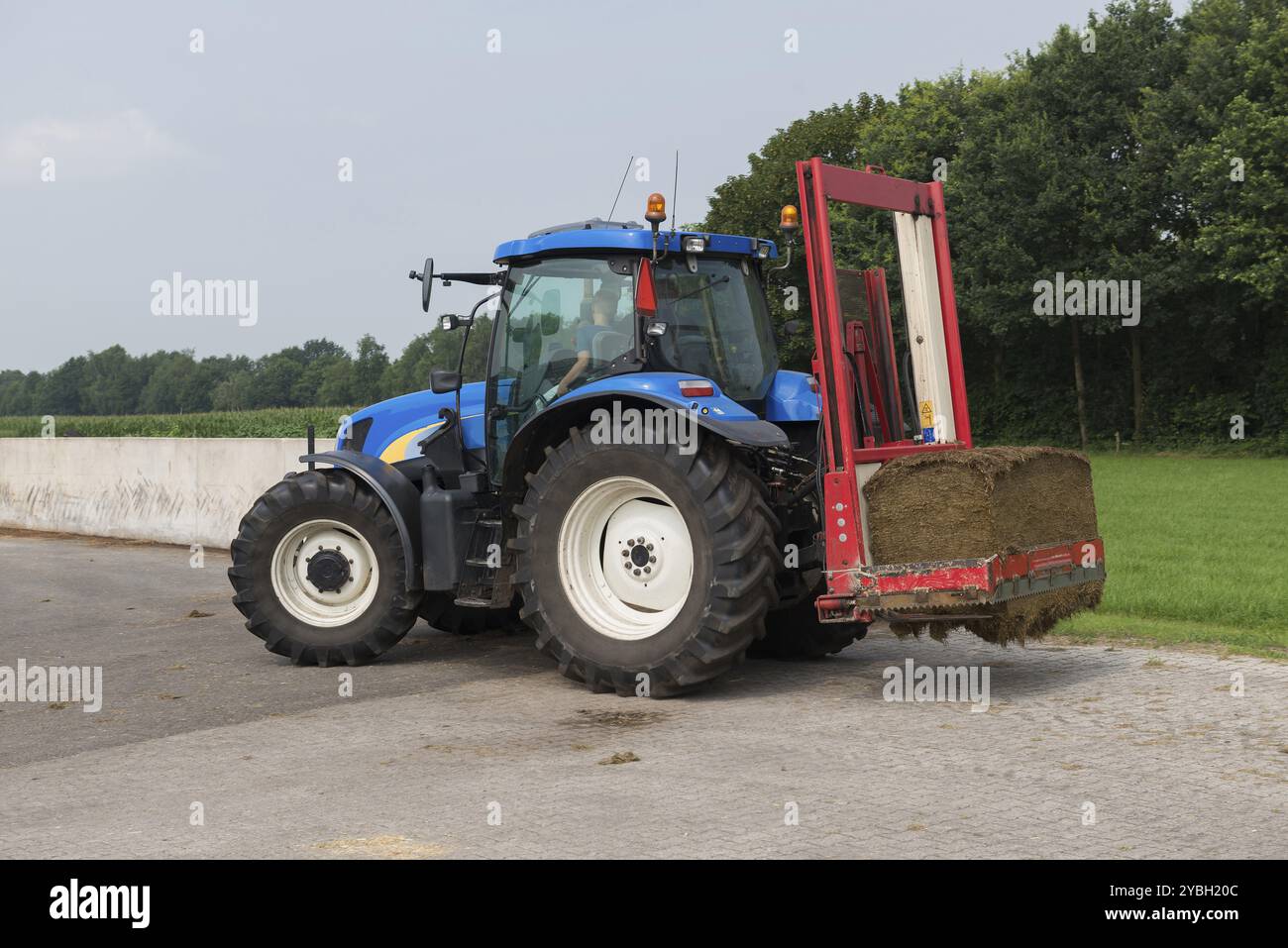 Blaue Traktor mit einem roten Ballen Hobel zum Abschneiden Silageballen Stockfoto