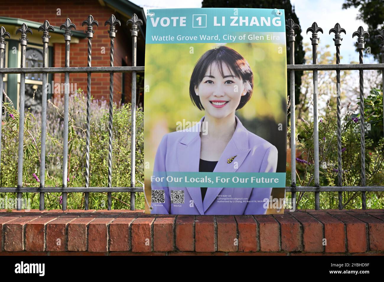 Wahlkampfschild für Li Zhang, einen Kandidaten bei der Kommunalwahl der Stadt Glen Eira, an einem Zaun befestigt, mit Garten und Haus im Hinterland Stockfoto