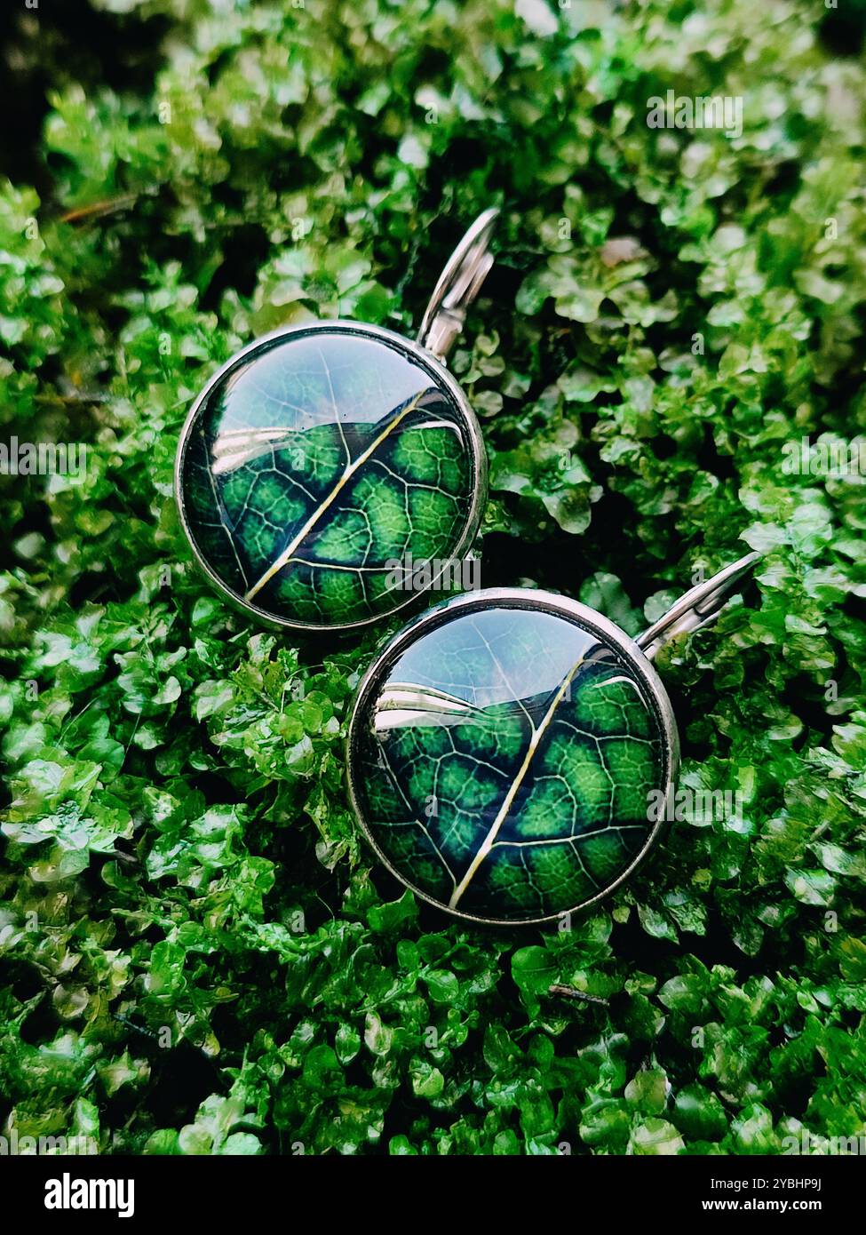 Handgefertigte Harz-Ohrringe echte grüne Blätter in einer transparenten Oberfläche auf grünem Moos Hintergrund geschlossen. Leverback Haken, naturinspirierter Schmuck - Smartphone-aufgenommenes Stockfoto