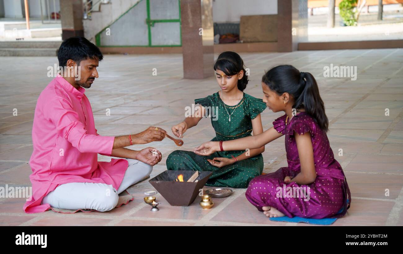 Eine indische Familie in traditioneller Kleidung führt eine Yagya oder Havan aus, die von einem Priester geleitet wird, um die Energien in ihrem Haus auszugleichen. Dieser heilige pooja ist für Harmonie Stockfoto