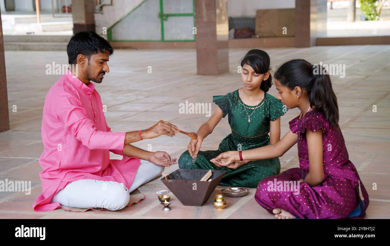 Eine indische Familie in traditioneller Kleidung führt eine Yagya oder Havan aus, die von einem Priester geleitet wird, um die Energien in ihrem Haus auszugleichen. Dieser heilige pooja ist für Harmonie Stockfoto