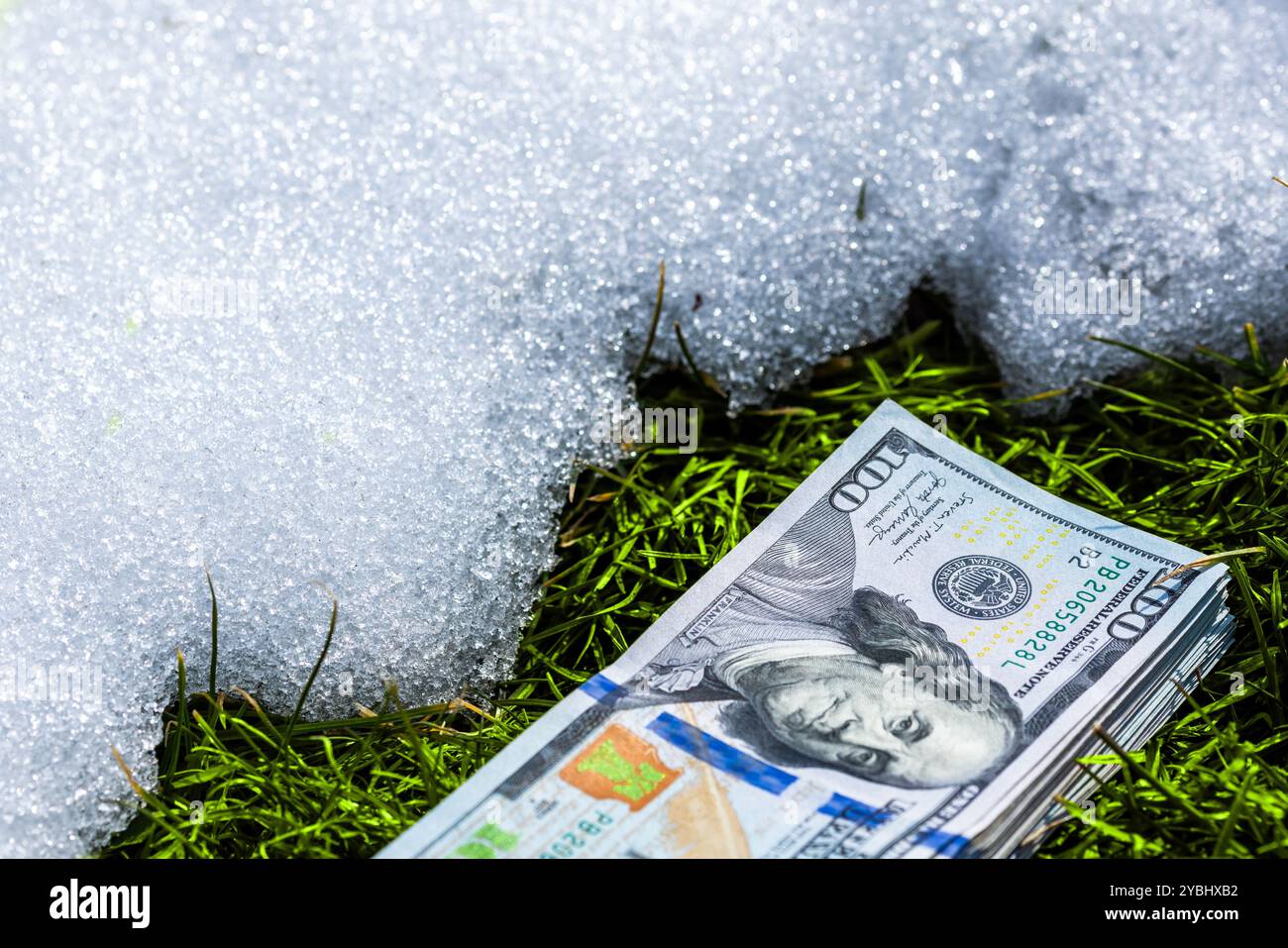 Ein Bündel Bargeld, das auf einer Schneeoberfläche in der Nähe von aufgetautem grünem Gras liegt und Themen wie Geldverschwendung und verpasste Gelegenheiten anschaulich veranschaulicht Stockfoto