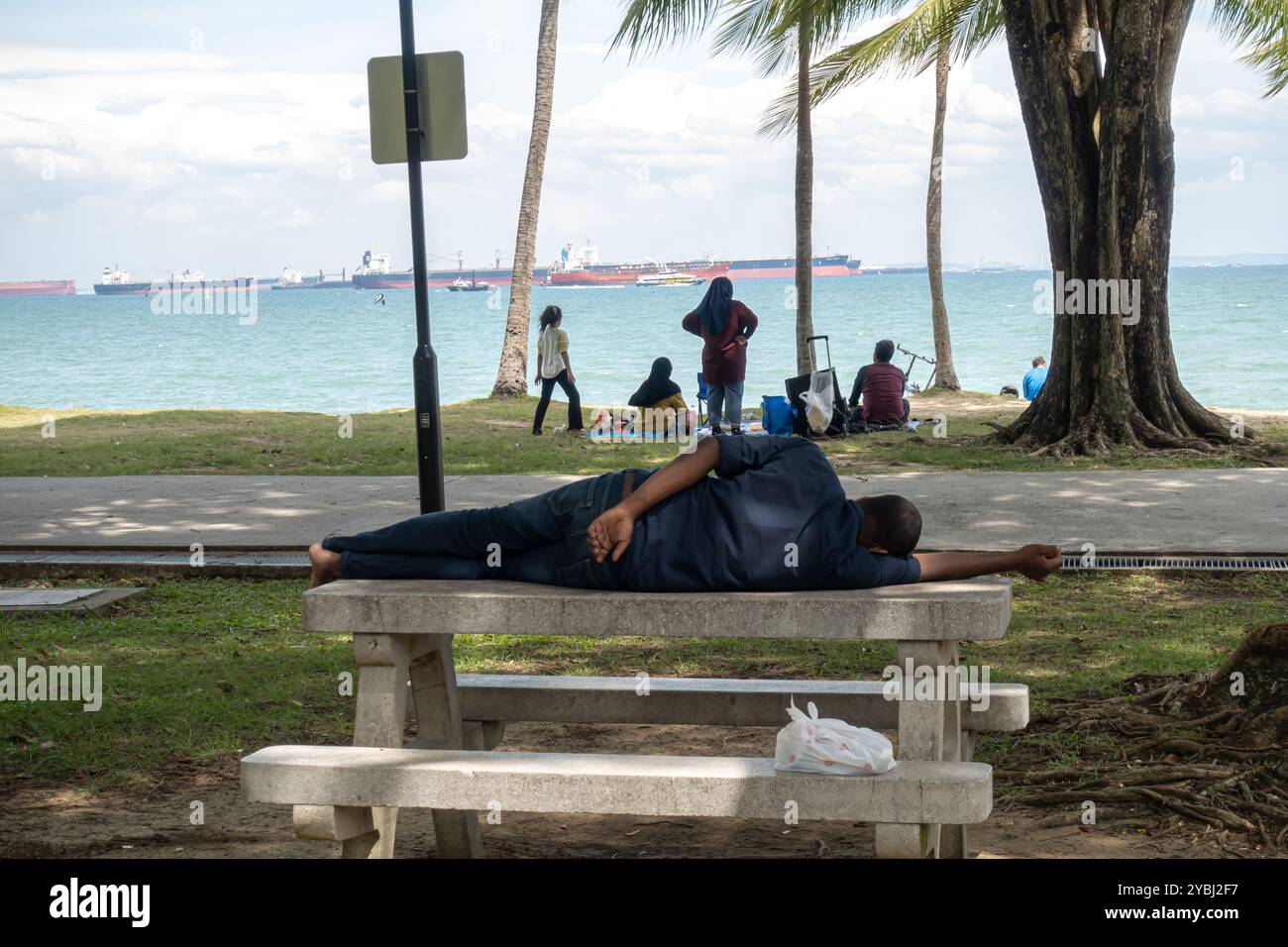 Ein Mann, der auf der Bank im East Coast Park, Singapur, Asien schläft. Leute, die ein Picknick machen Stockfoto