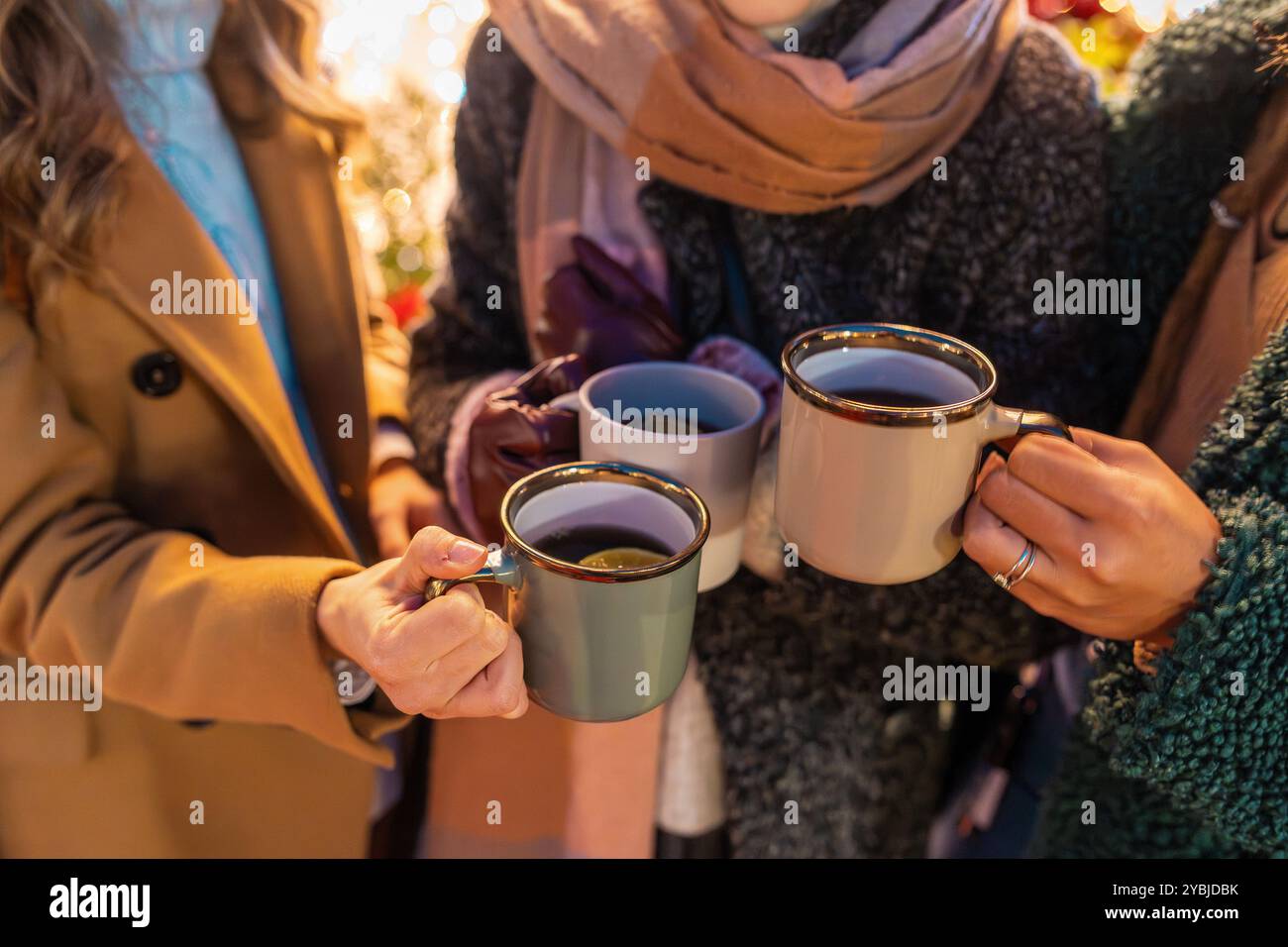 Nahaufnahme von Händen, die Tassen mit heißen Getränken auf einem Weihnachtsmarkt halten. Freunde genießen warme Getränke, tragen Wintermode. Gemütliche und festliche Atmosphäre Stockfoto