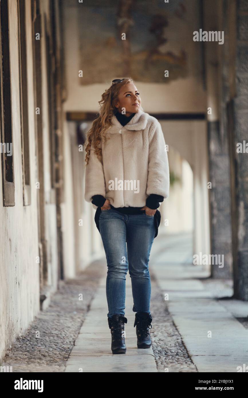Eine junge Frau mit langen, blonden Haaren schlendert fröhlich durch ein bezauberndes europäisches Stadtzentrum und bestaunt die atemberaubende Architektur Stockfoto
