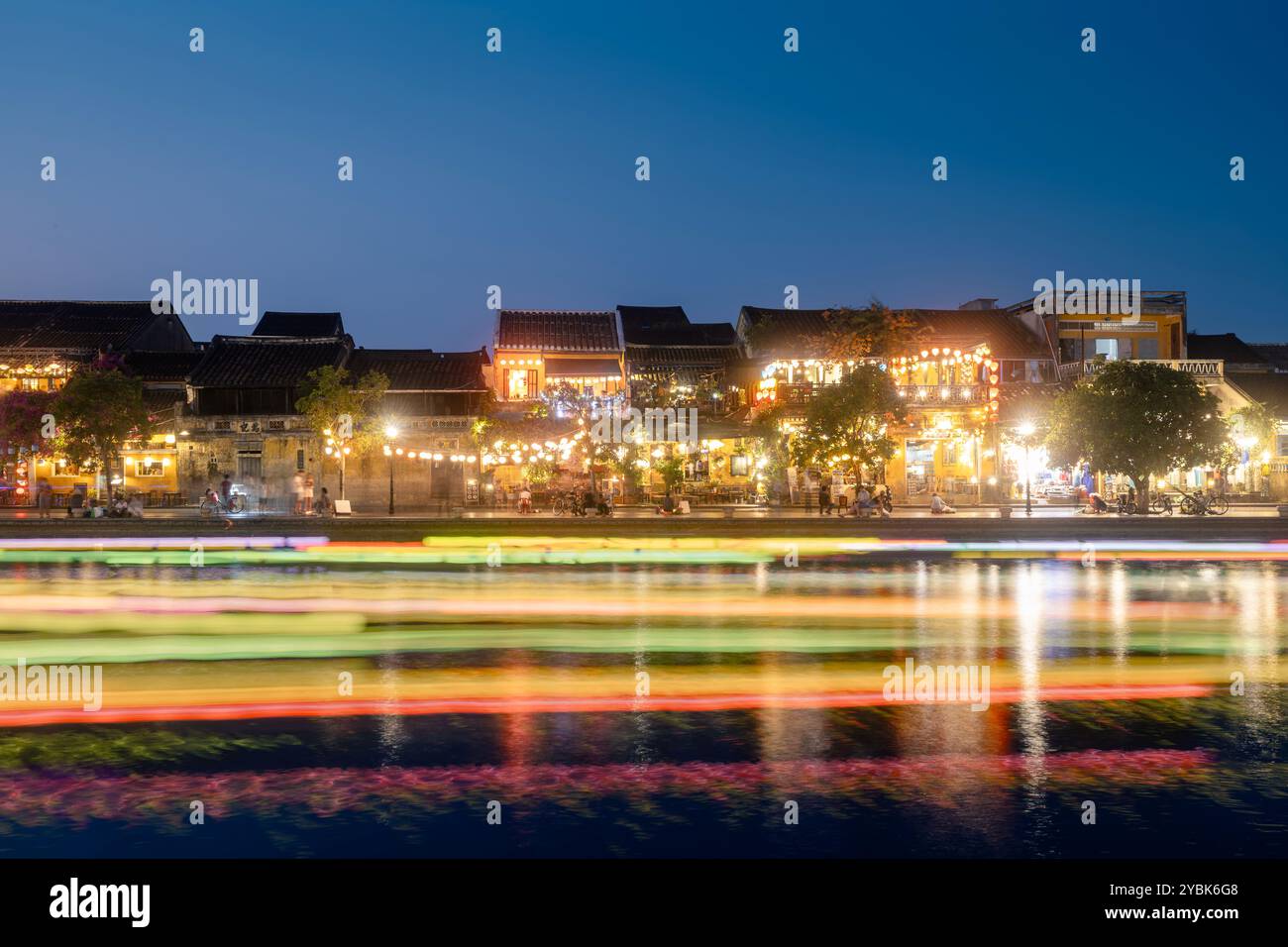 Leichte Spuren von Booten mit traditionellen Laternen auf der Fahrt. Nächtliche Szene des Wasserkanals und der Uferpromenade in der antiken Stadt Hoi an in Vietnam. Stockfoto