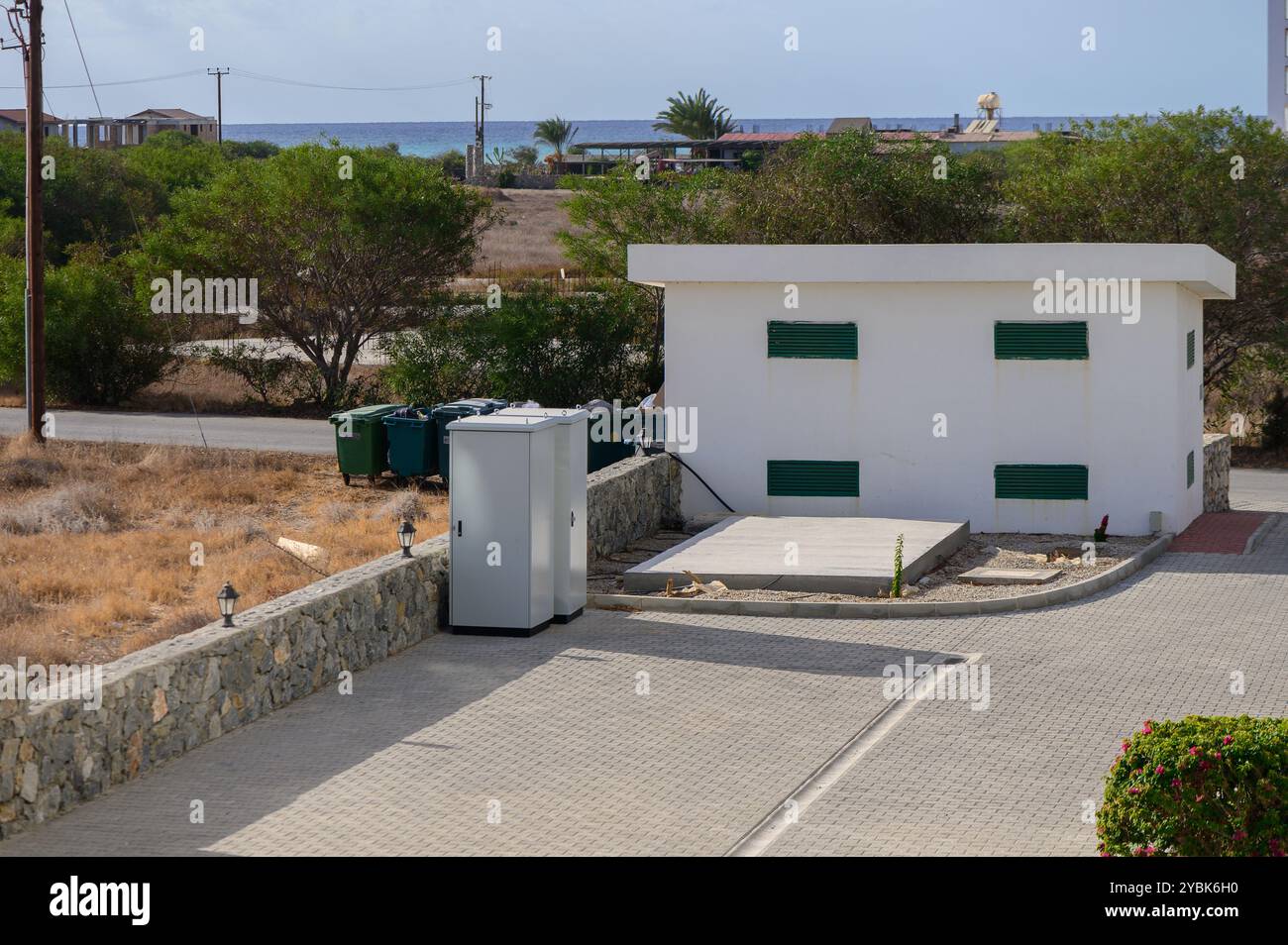 Die scharf weiße Struktur steht vor einem Hintergrund von üppigem Grün und Blick auf das ferne Meer und verkörpert Ruhe an einem hellen Tag. Stockfoto