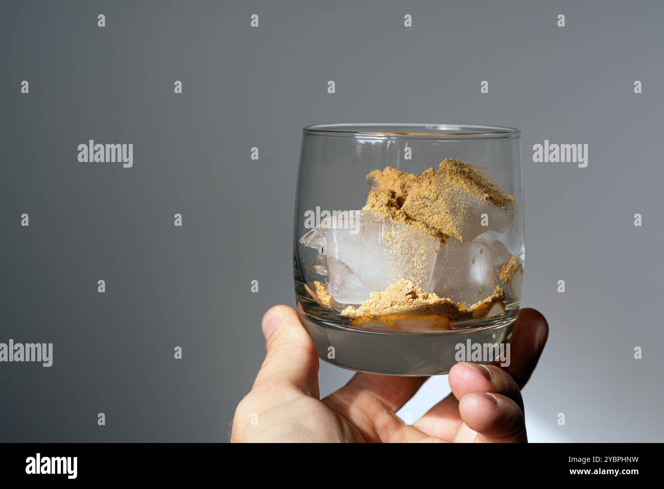 Ein Glas gefüllt mit Eiswürfeln und gepudertem Amanita Muscaria Pilz auf der Oberfläche, in der Hand gehalten und von natürlichem Sonnenlicht beleuchtet. Stockfoto