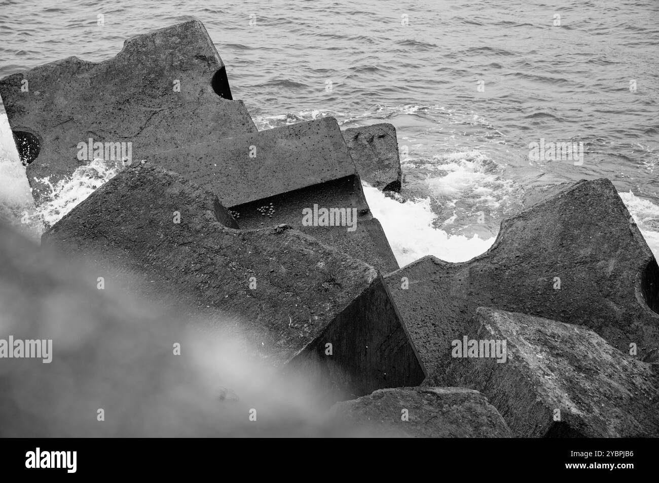 Schwarz-weiß-Bild von geometrischen Betonblöcken an der Seixal-Küste, die als Wellenbrecher gegen die Wellen des Atlantischen Ozeans entworfen wurden Stockfoto