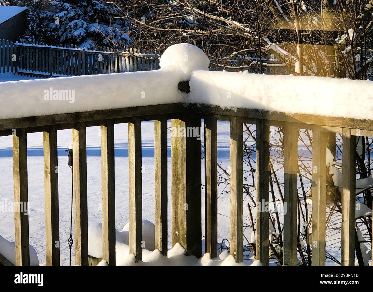 Am späten Nachmittag wirft die Sonne lange Schatten auf den frischen, weißen Schnee, der sich zu Beginn des Winters auf den Geländern und Pfosten eines Hinterhofdecks aufbaut. Stockfoto