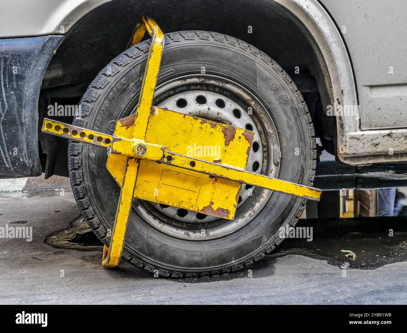 Nahaufnahme einer gelben Radklemme, die den Reifen eines geparkten Fahrzeugs sichert, symbolisiert Strafverfolgung, Konsequenzen und Parkverstöße Stockfoto
