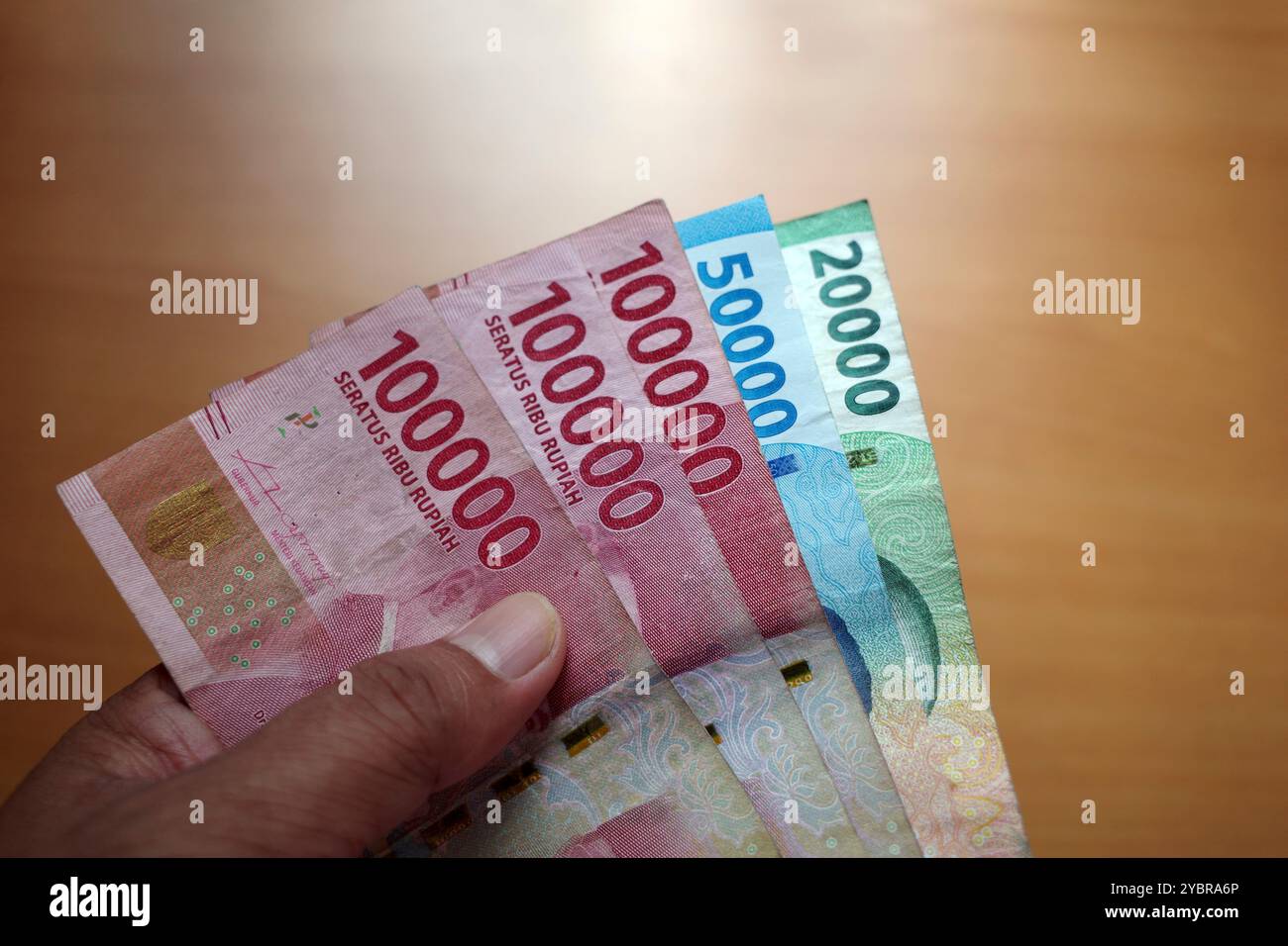 Erwachsener Finger hält Rupiah, indonesisches Geld mit unscharfem braunem Hintergrund. Sparen und Geben des Konzepts Stockfoto