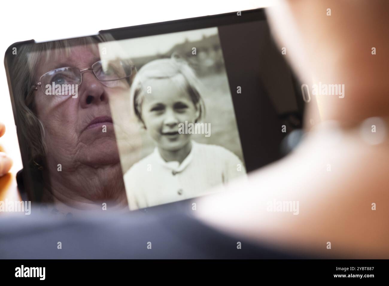 Ältere kaukasische Frau, die alte Fotos von sich selbst als junge Frau auf einem Tablet-Computer betrachtet, kontrastiert den Alterungsprozess Nostalgie und Chi Stockfoto