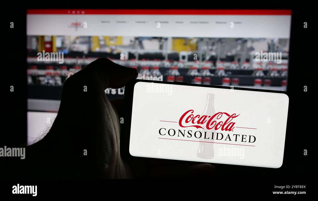 Person, die ein Mobiltelefon mit dem Logo der amerikanischen Firma Coca-Cola Consolidated Inc. Auf dem Bildschirm vor der Webseite hält. Schwerpunkt auf dem Display des Telefons. Stockfoto